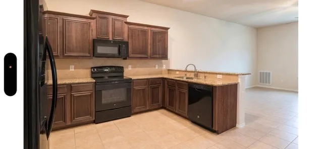 Kitchen featuring wood-finish cabinetry, granite-style countertops, and beige tile flooring