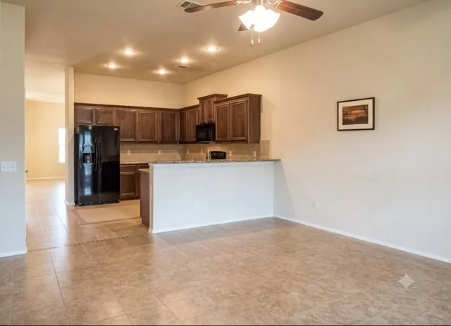 Open-concept kitchen and living area featuring tile flooring, dark wood cabinetry, a breakfast bar, recessed lighting, and a ceiling fan