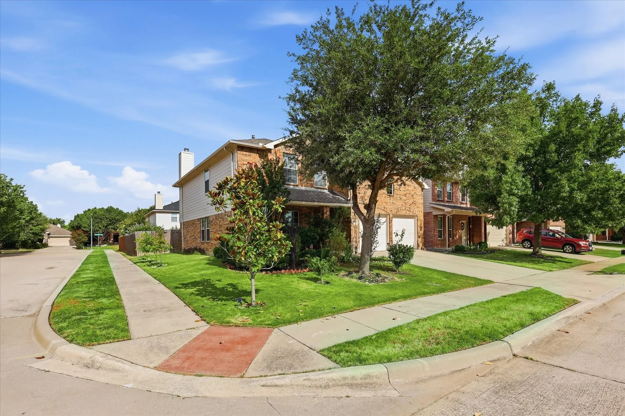 Traditional brick and siding exterior featuring a manicured lawn, established trees, an attached garage, and a concrete driveway