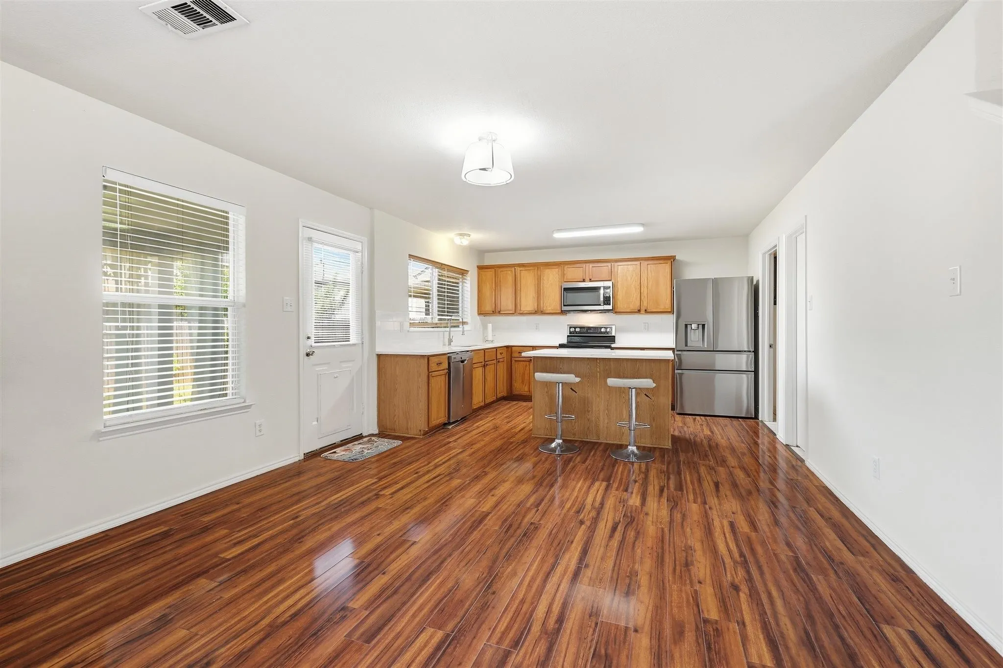 Open-concept living space featuring wood-finish flooring, a kitchen island with seating, stainless steel appliances, and wood cabinetry