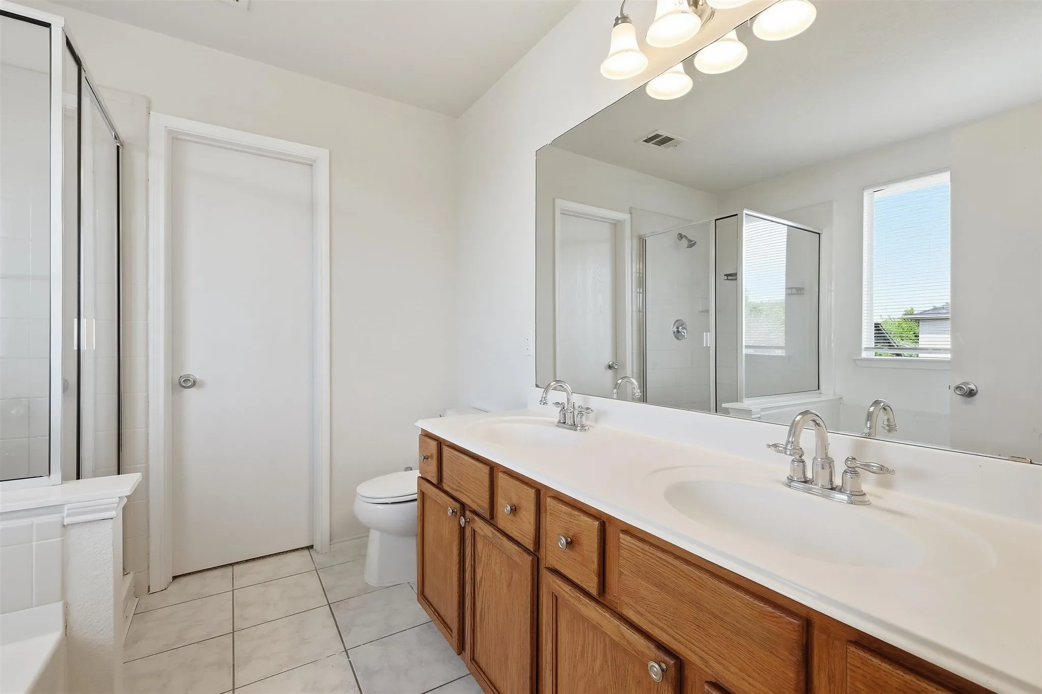 Bathroom with a double vanity featuring a light wood-finish cabinet and two integrated sinks