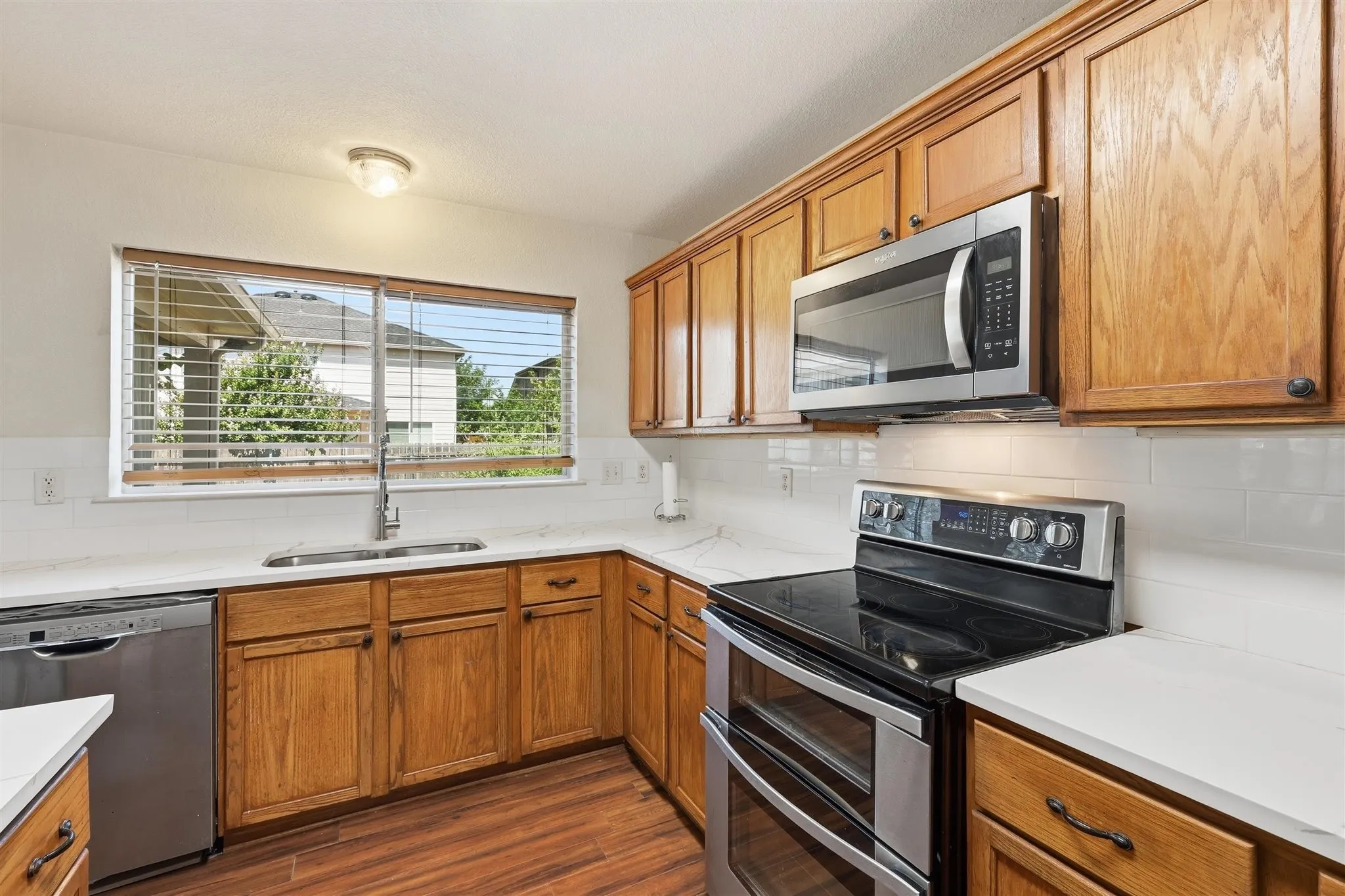 Kitchen featuring wood-finish cabinetry, stainless steel appliances, a double basin sink, white countertops, and a white subway tile backsplash