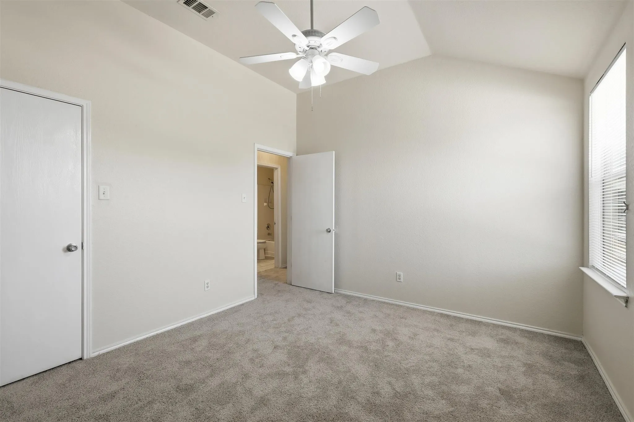 Spacious room featuring vaulted ceilings, neutral-toned walls, and plush grey carpeting