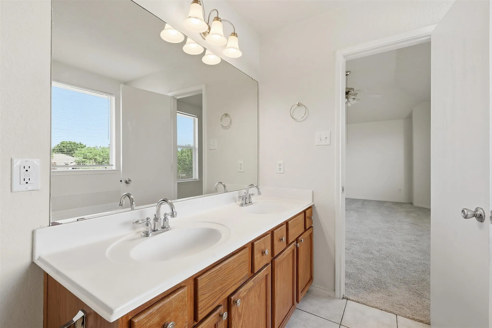 Bathroom vanity featuring dual sinks with chrome fixtures, a spacious countertop, and wood-finish cabinetry