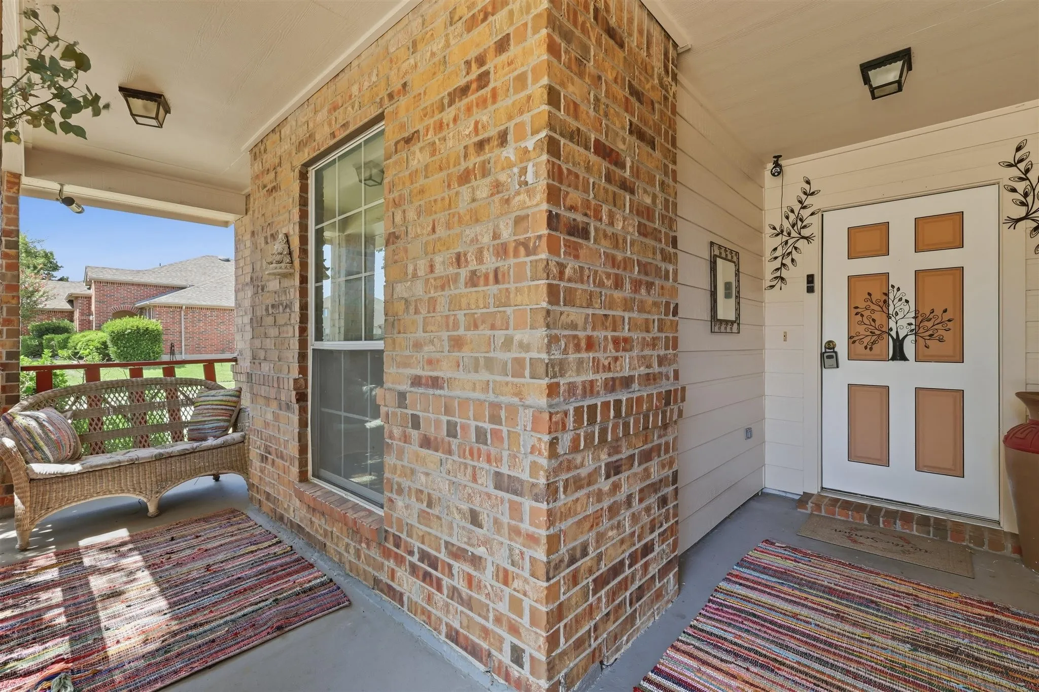 Covered front porch featuring brick and siding exterior, a multi-pane window, and a paneled entry door with decorative glass inserts