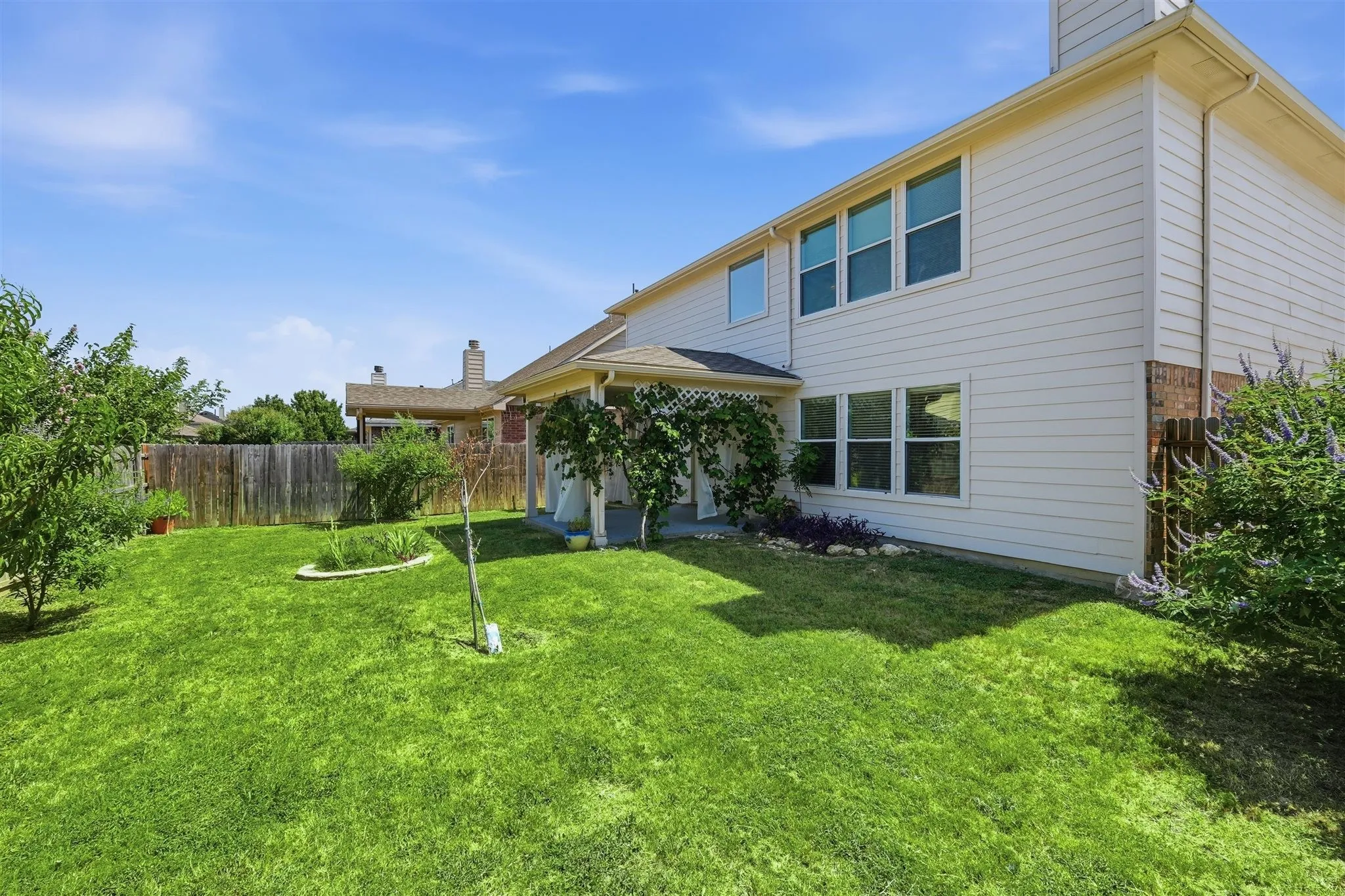 Spacious backyard featuring a covered patio, extensive lawn, mature trees, and privacy fencing