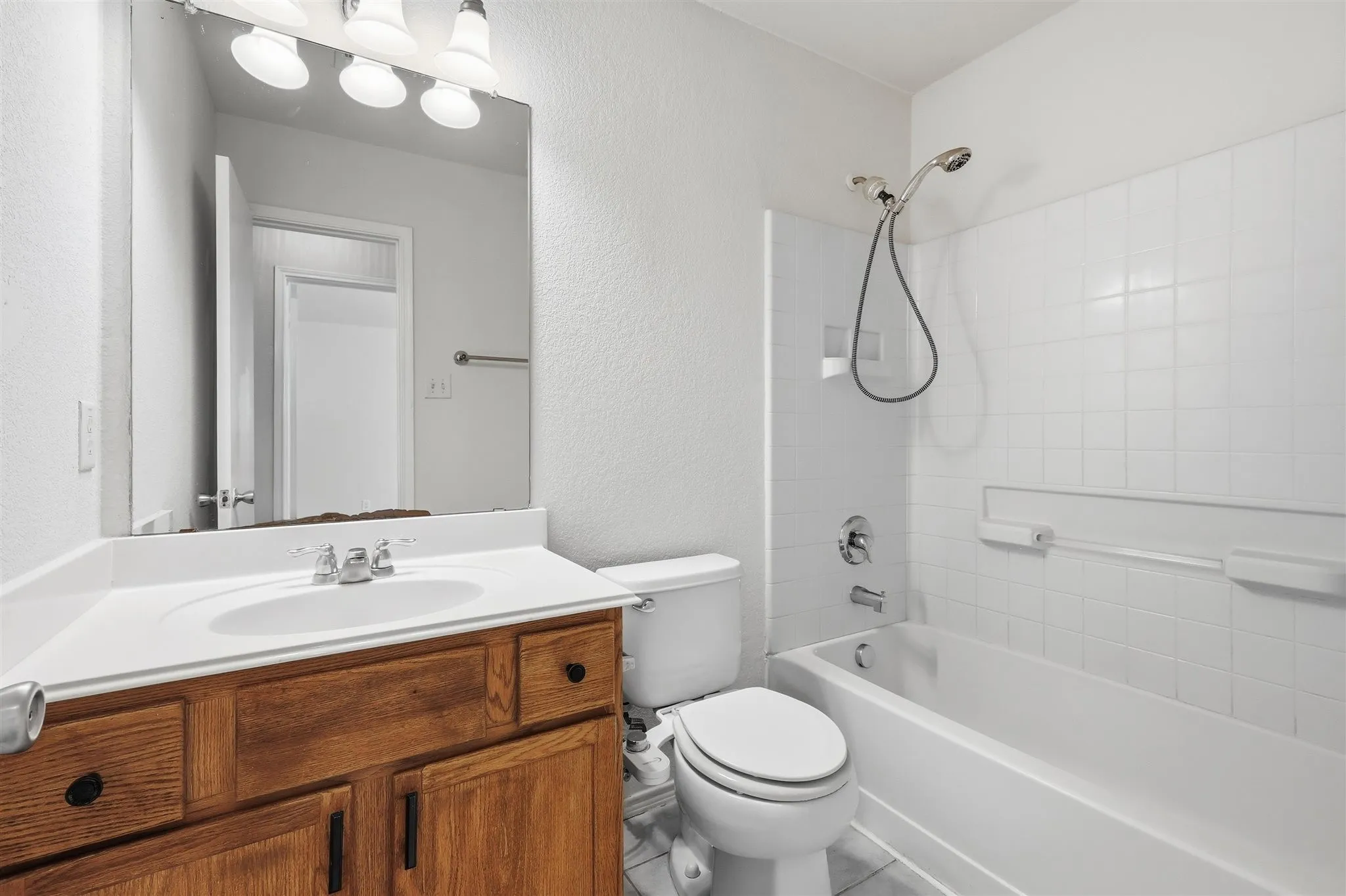 Bathroom featuring a wood-finish vanity with a white countertop and integrated sink, a large mirror, and a three-bulb vanity light fixture