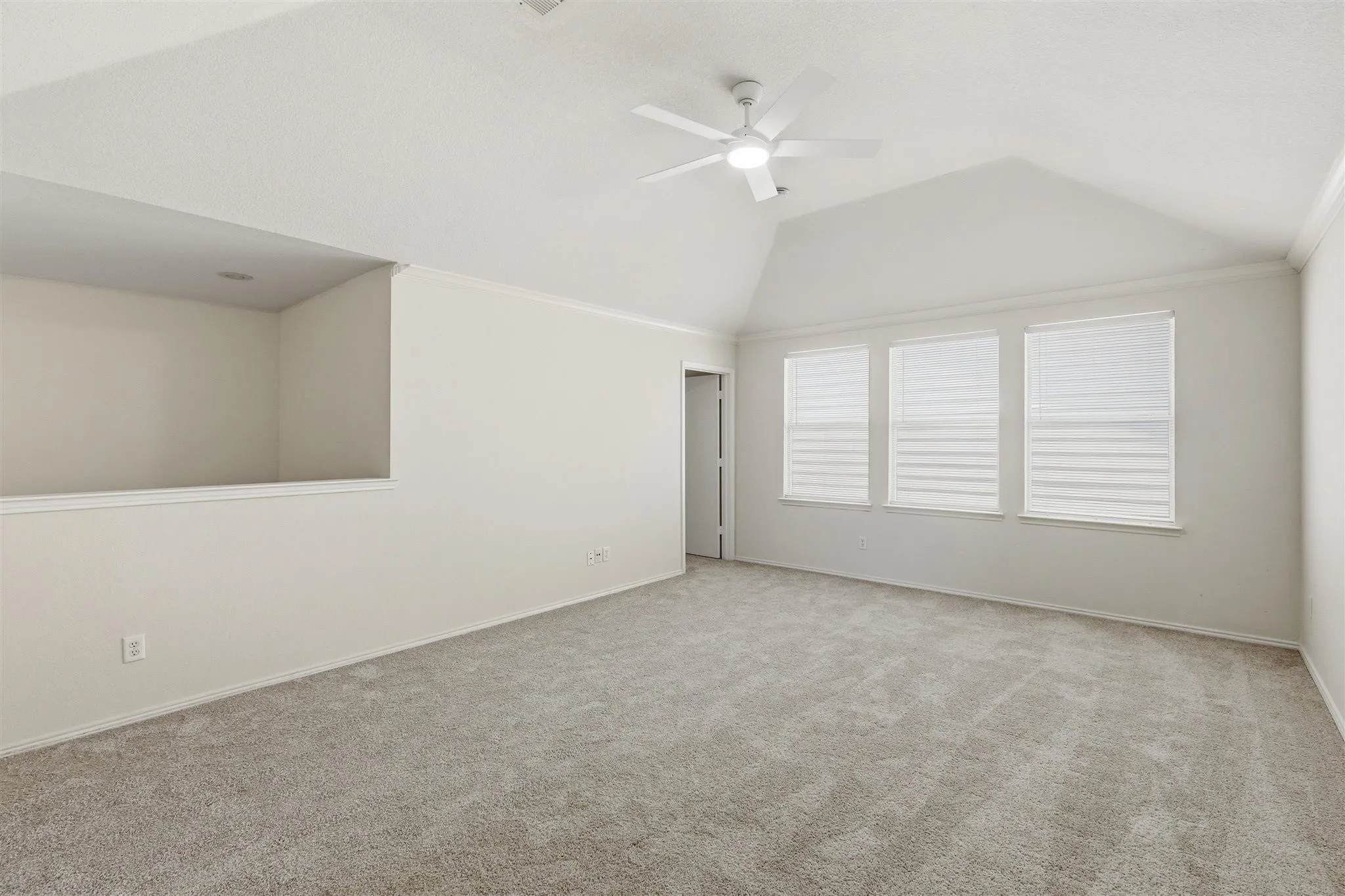 Spacious room featuring vaulted ceilings, three windows with horizontal blinds, neutral wall paint, and plush carpeting