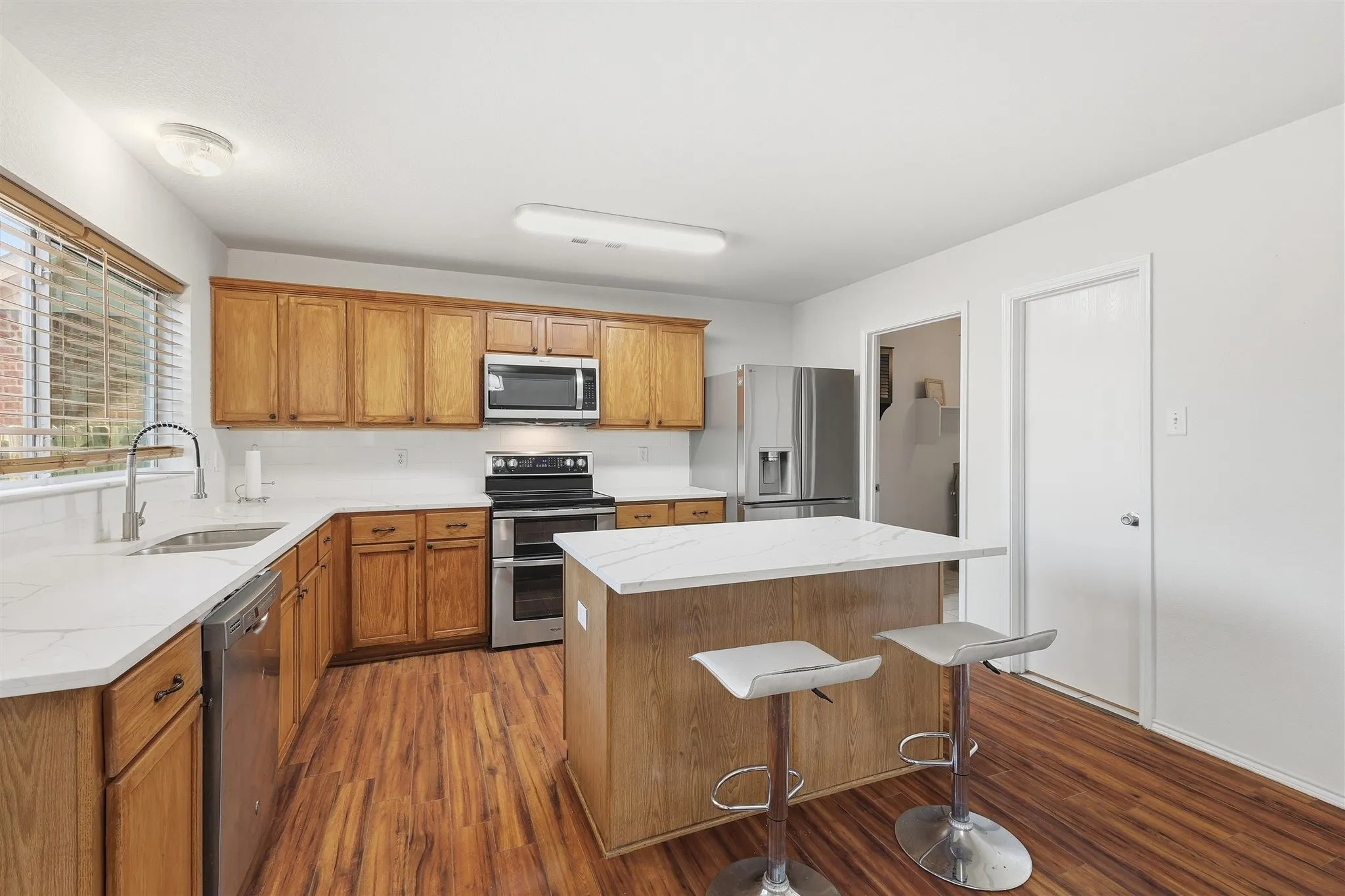 Kitchen featuring wood-finish flooring, wood cabinetry, white countertops, stainless steel appliances, and a central island with seating