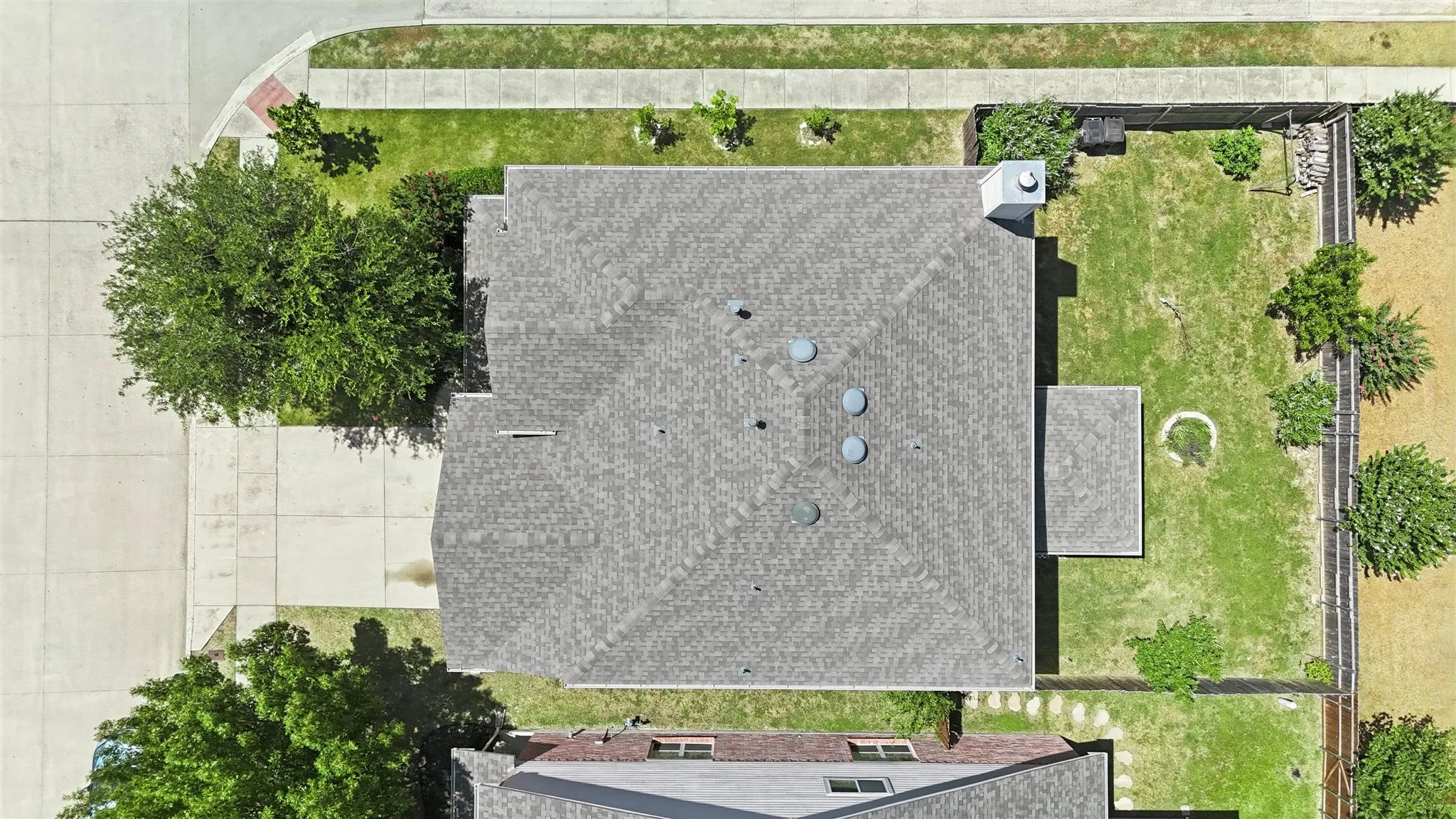 Aerial overview showcasing a shingled roof, a concrete driveway, and a spacious fenced backyard