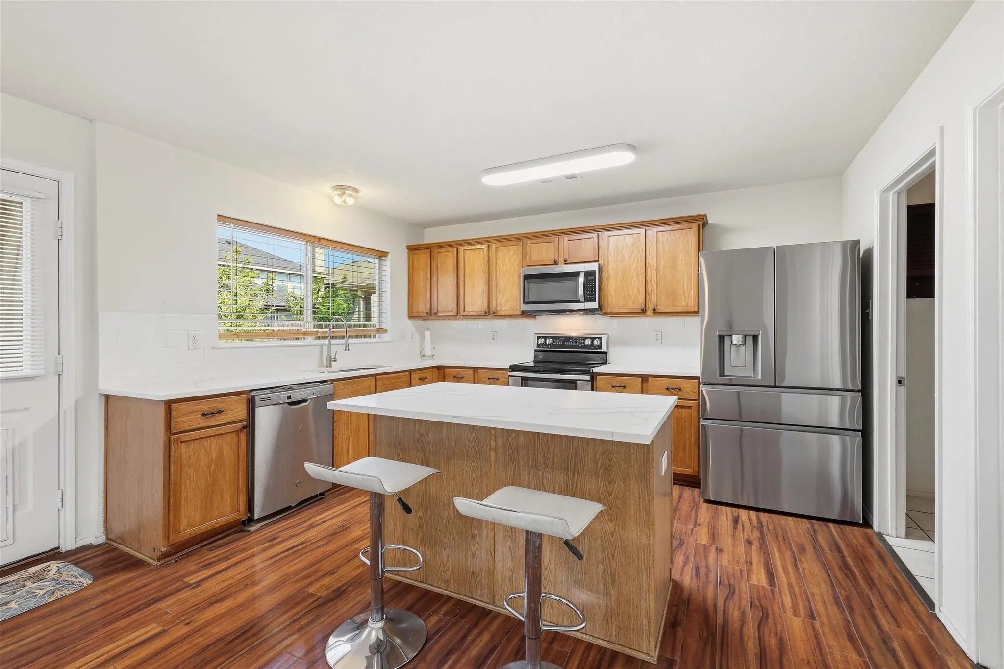 Kitchen featuring wood-finish flooring, an island with countertop seating, stainless steel appliances, light-toned countertops, and ample cabinetry