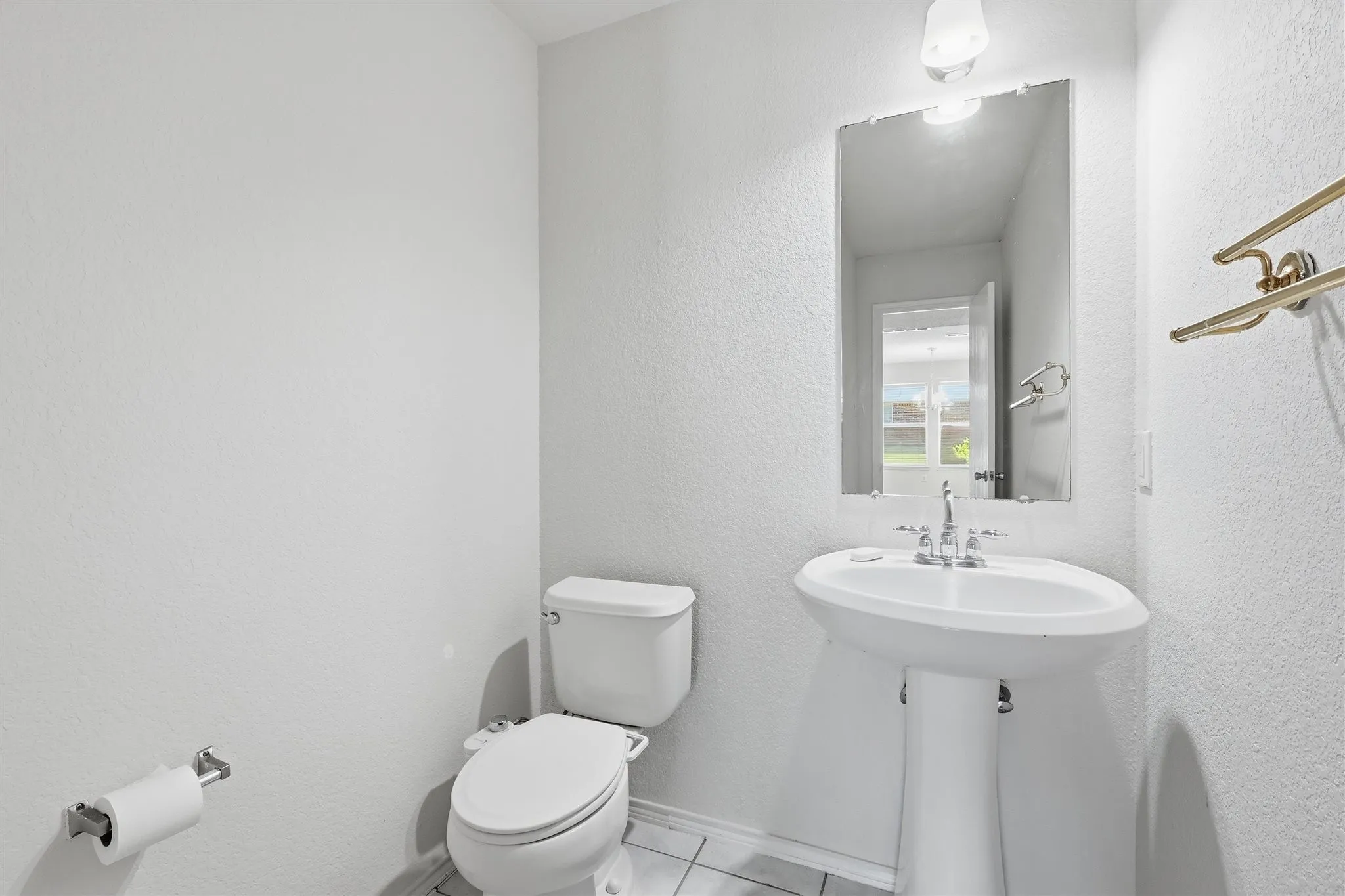 Powder room featuring a pedestal sink, wall-mounted mirror, white toilet, and tile flooring