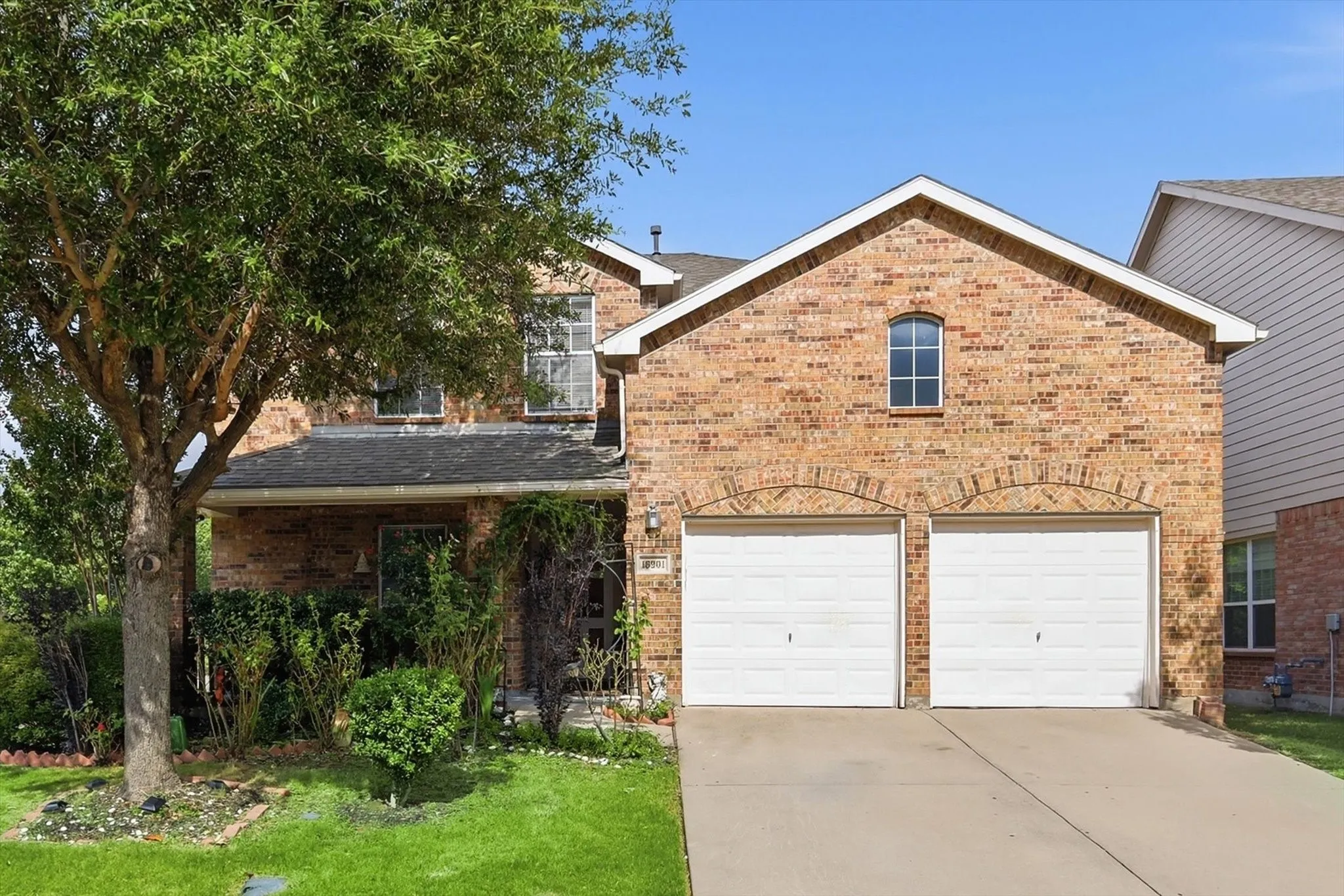 Brick facade residence featuring a two-car garage with arched brick detailing, a concrete driveway, and a gabled roofline