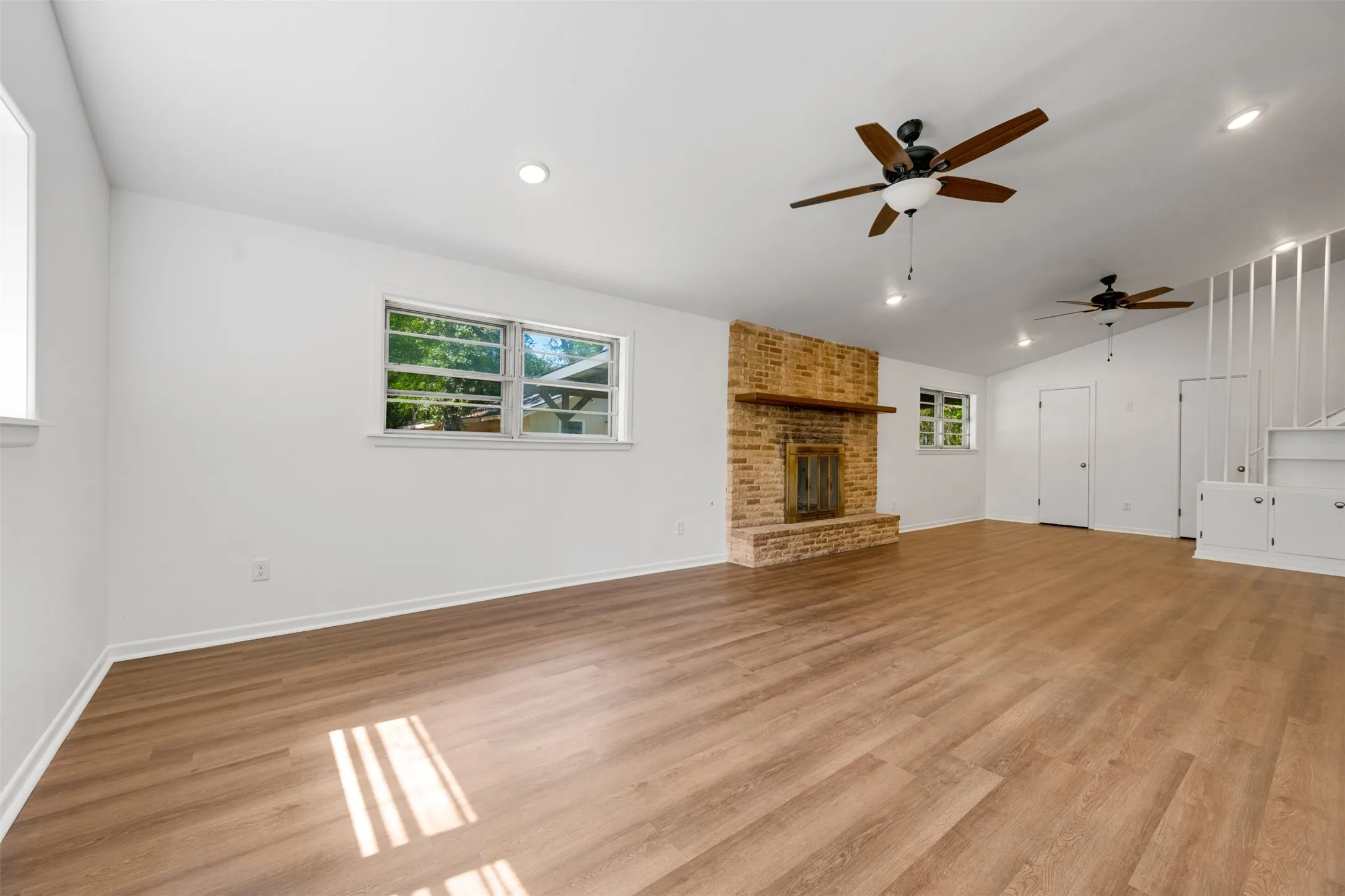Spacious living area featuring wood-finish flooring, a brick-surround fireplace with a wood mantle, and multiple windows