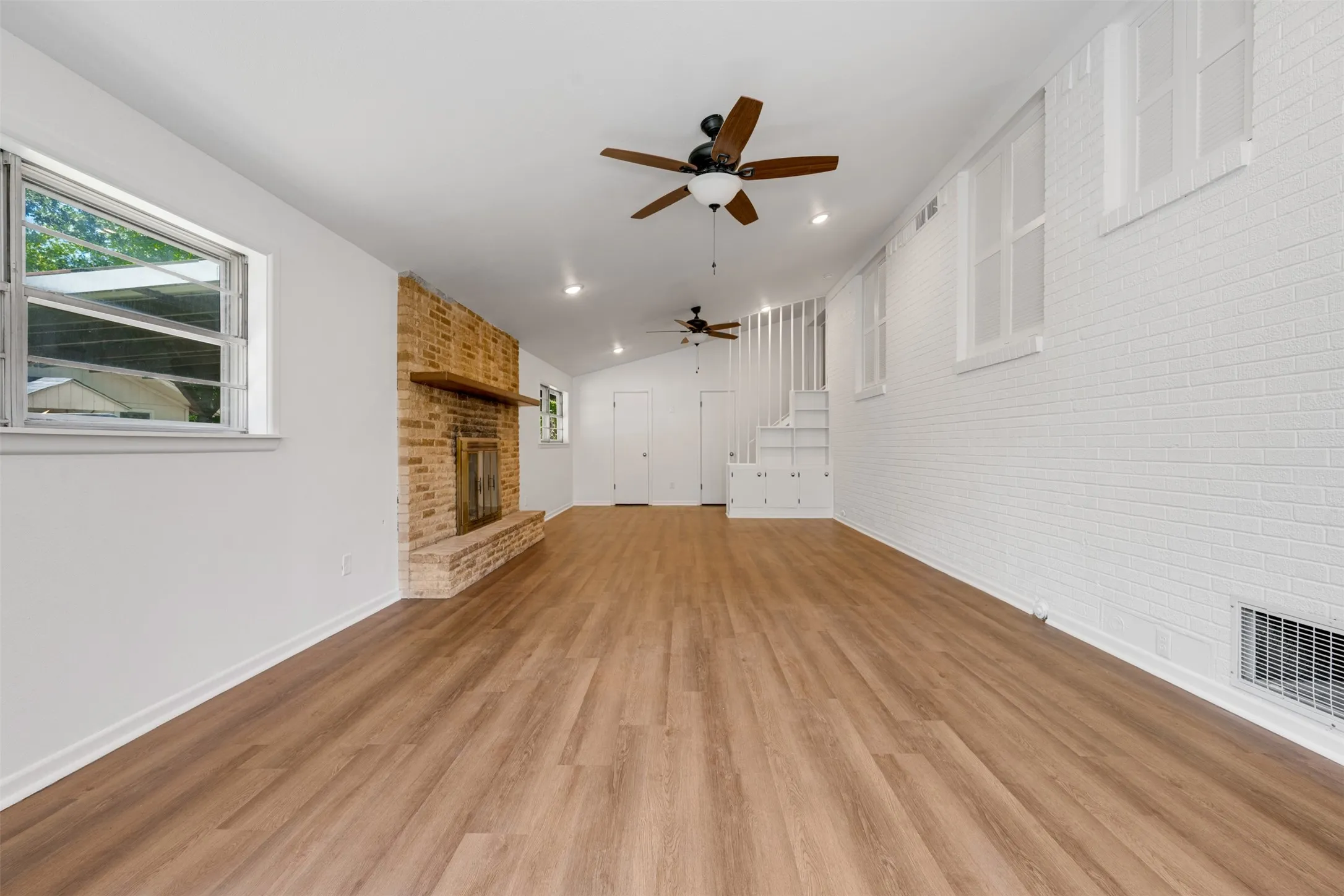 Spacious interior featuring wood-finish flooring, a brick fireplace with a wood mantle, and white painted brick walls