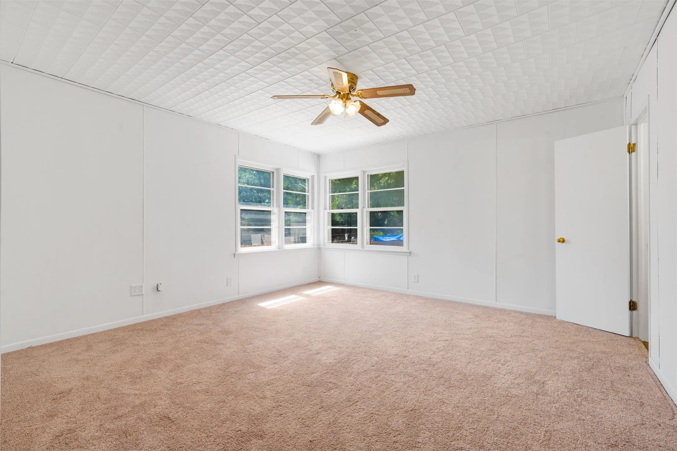 Room featuring light tan carpeting, white paneled walls, and a white patterned ceiling