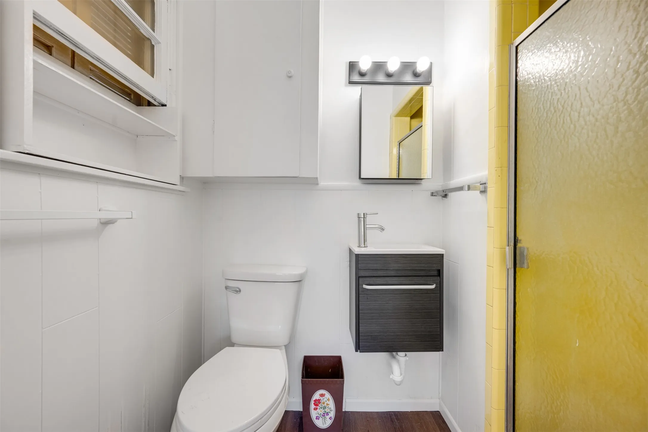 Compact bathroom featuring a shower with a textured glass door, a floating vanity with a single basin, a wall-mounted medicine cabinet, and white paneled walls
