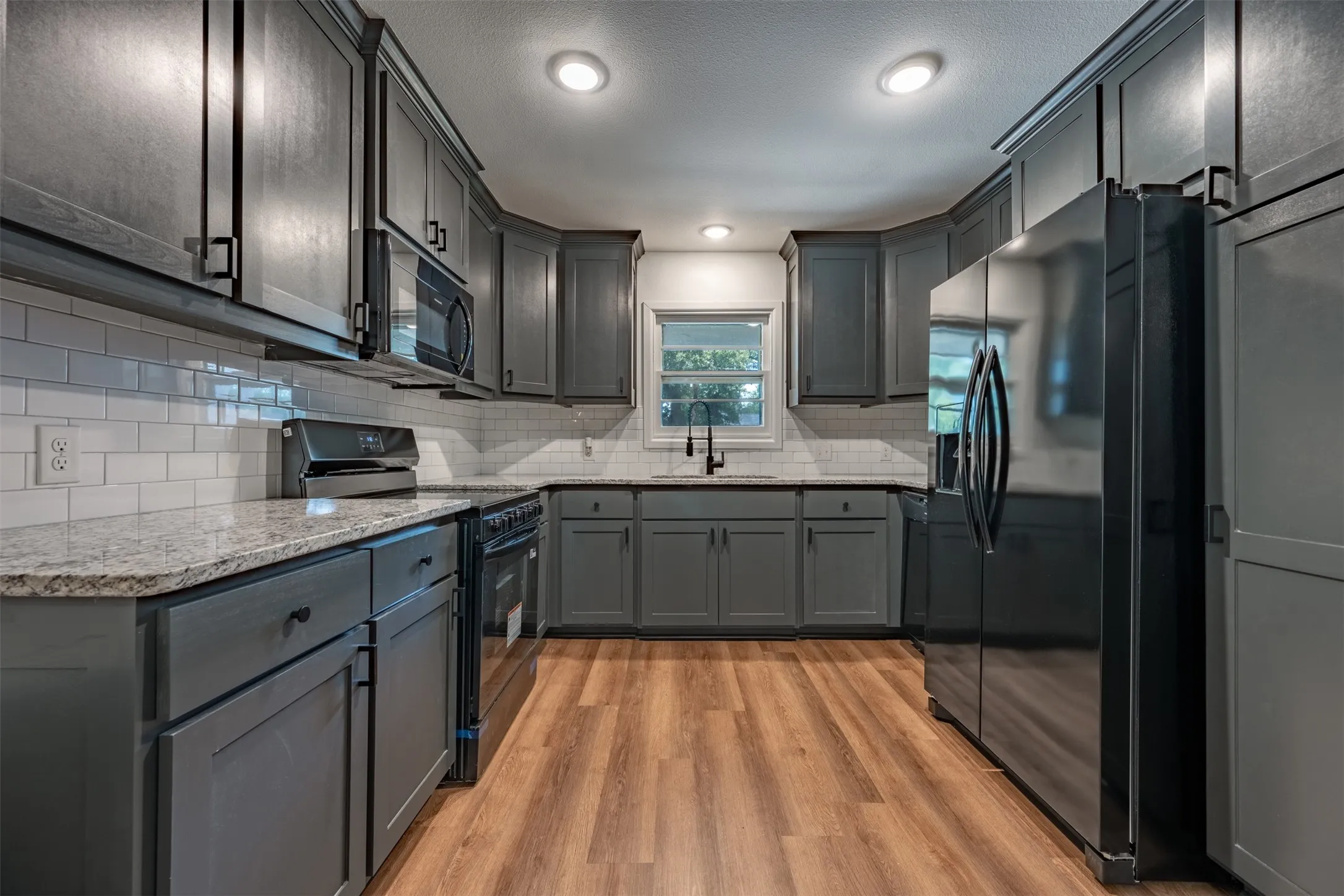 Kitchen featuring dark gray cabinetry, light-toned countertops, white subway tile backsplash, stainless steel appliances, and wood-finish flooring