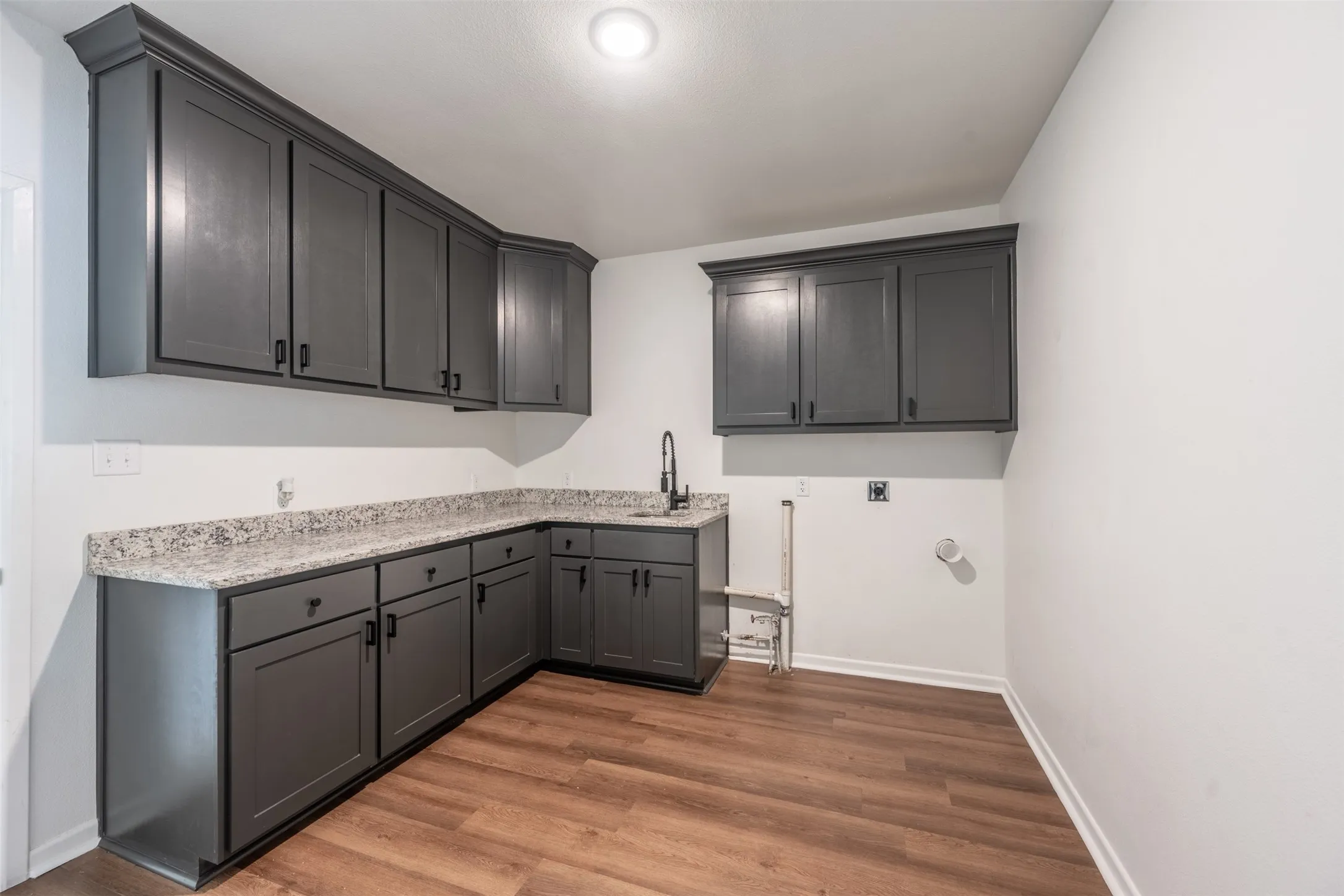 Corner sink with a matte black faucet, dark wood-finish flooring, white walls, and dark gray cabinetry with black​​‌​​​​‌​​‌‌​‌‌​​​‌‌​‌​‌​‌​​​‌​​ hardware