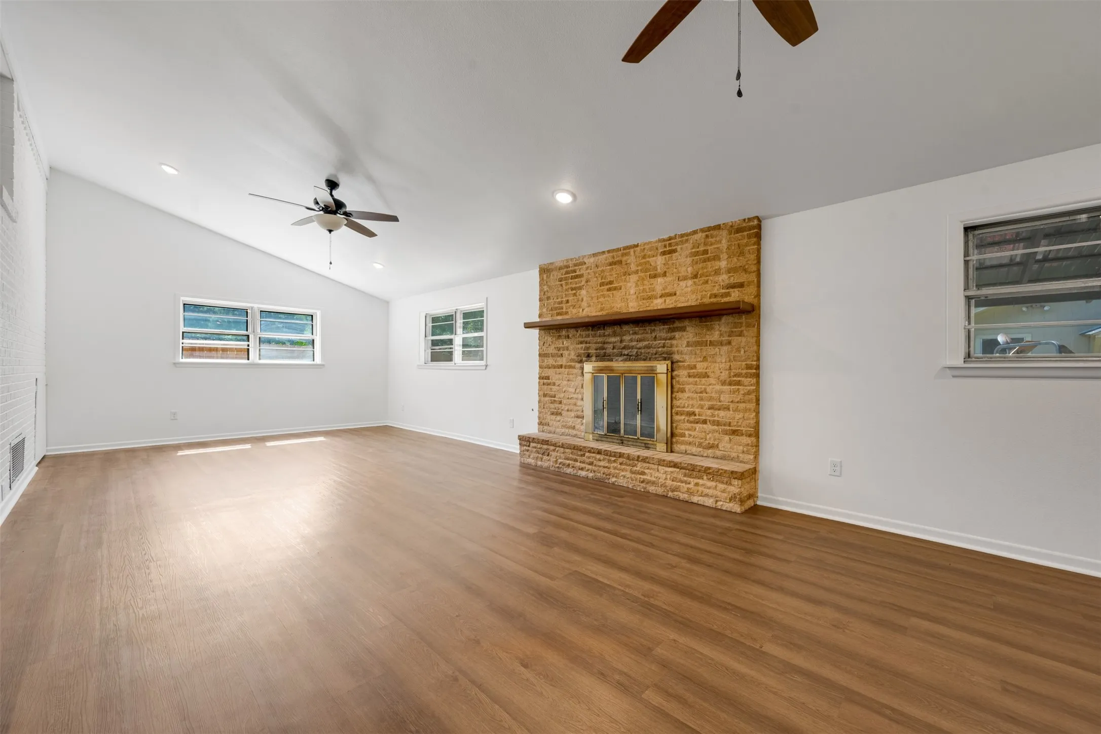 Living area featuring a floor-to-ceiling brick fireplace with a wood mantel, wood-finish flooring, and multiple ceiling fans