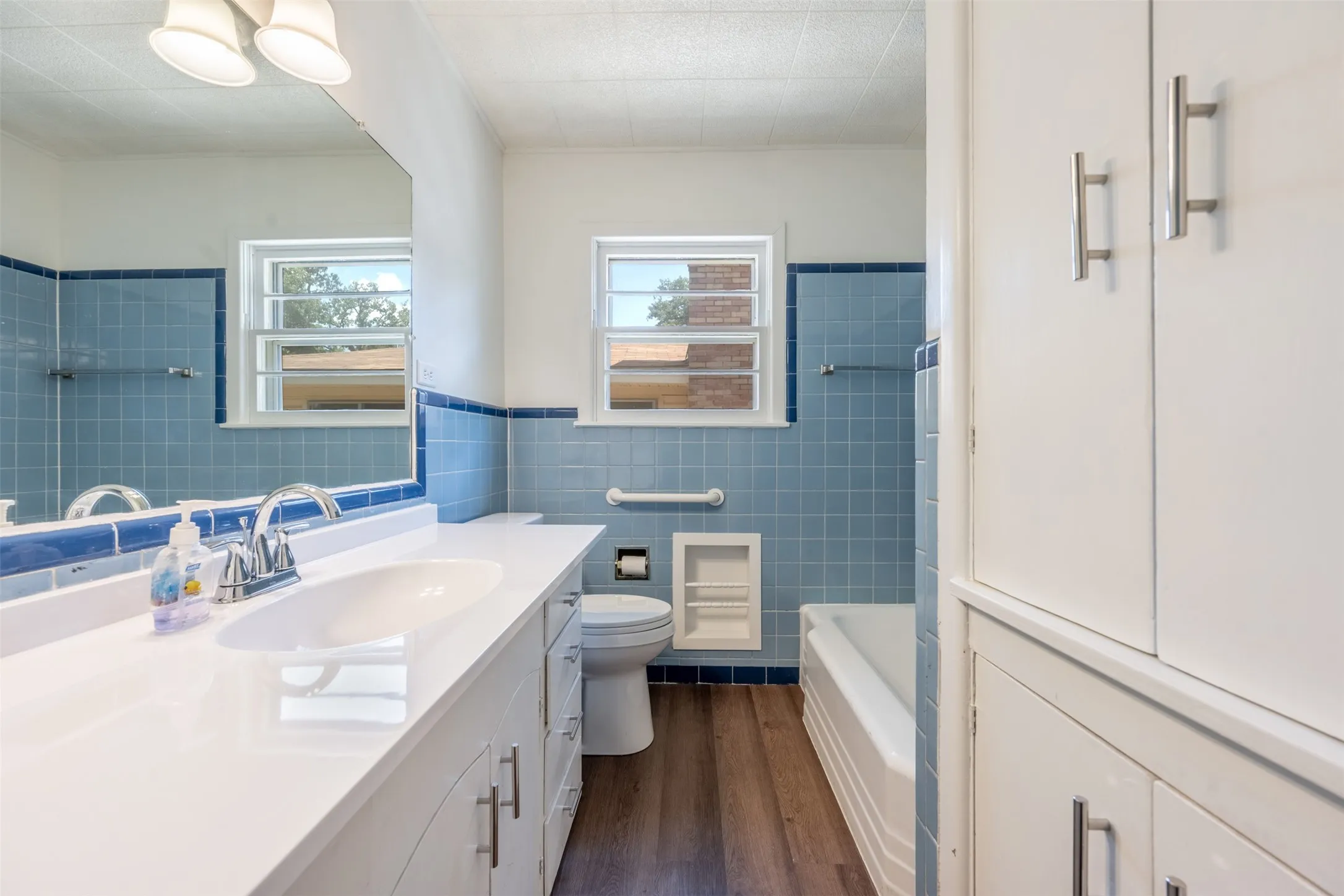 Bathroom featuring a spacious vanity with an integrated sink, built-in storage cabinetry, wood-finish flooring, and blue tile accents