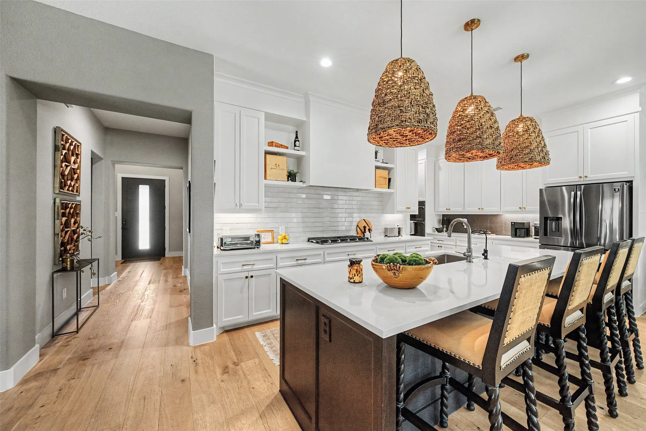 Gourmet kitchen featuring a large island with seating, pendant lighting, white cabinetry, integrated stainless steel appliances, and wood-finish flooring