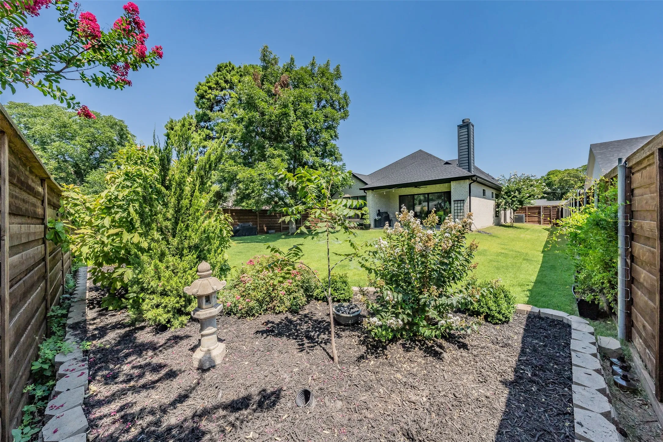 Expansive backyard featuring a manicured lawn, established landscaping, and a privacy fence