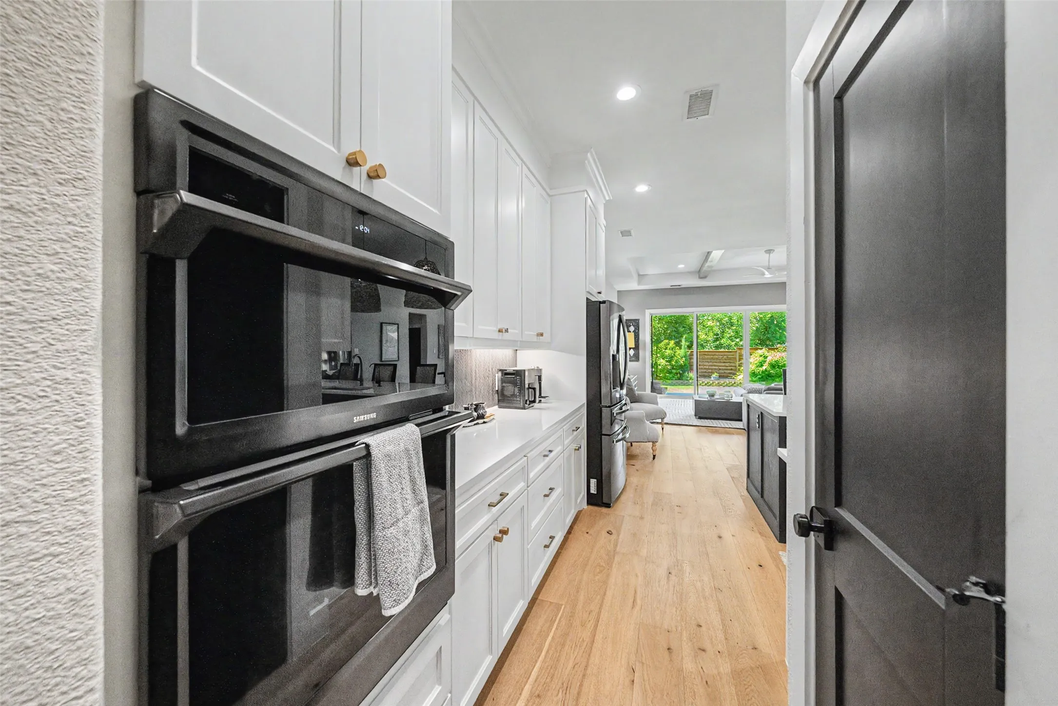 Double wall oven, white shaker cabinetry with gold-tone hardware, light wood-finish flooring, white countertop, and built-in refrigerator