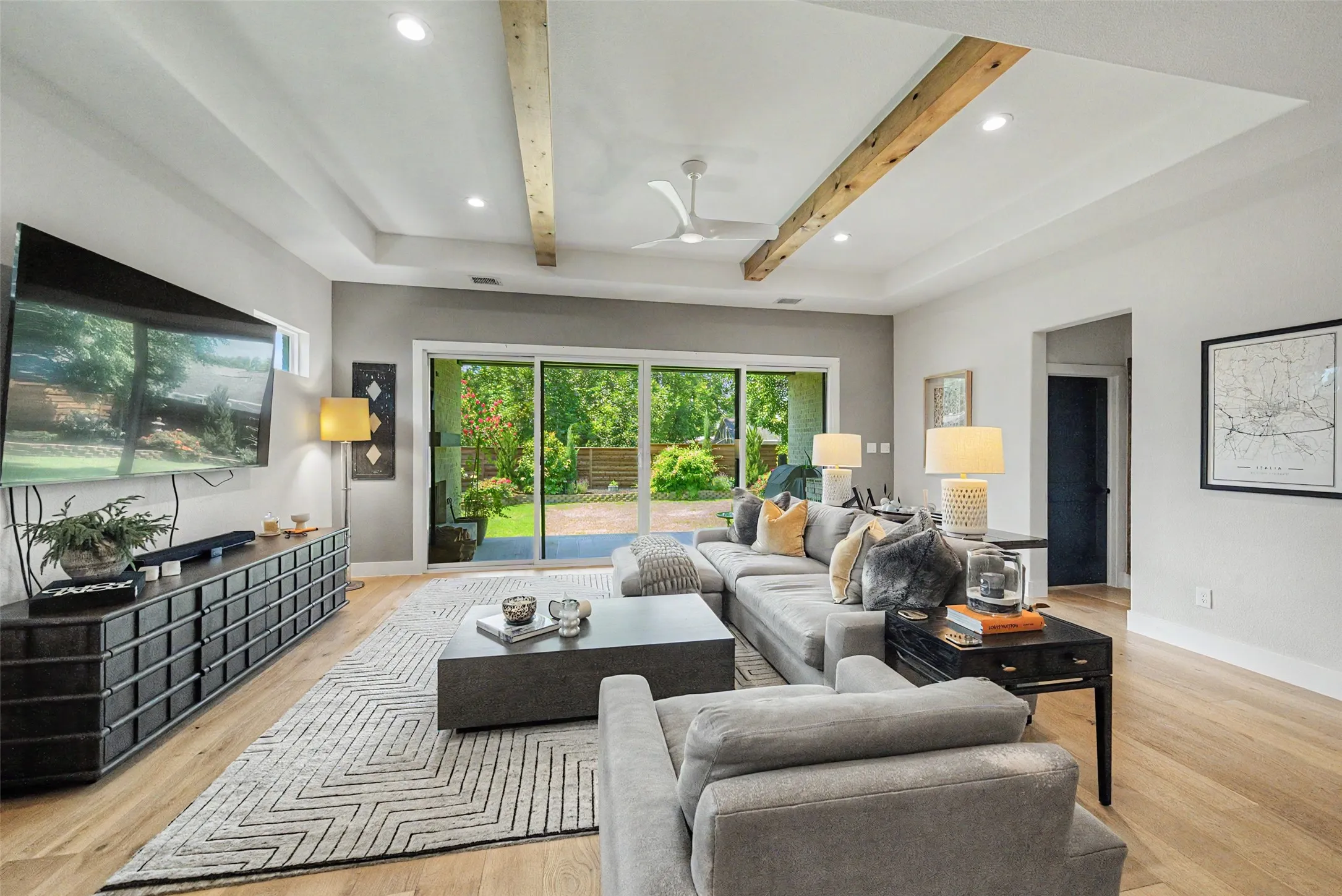 Spacious living area featuring light wood-finish flooring, a tray ceiling with exposed wood beams, and recessed lighting