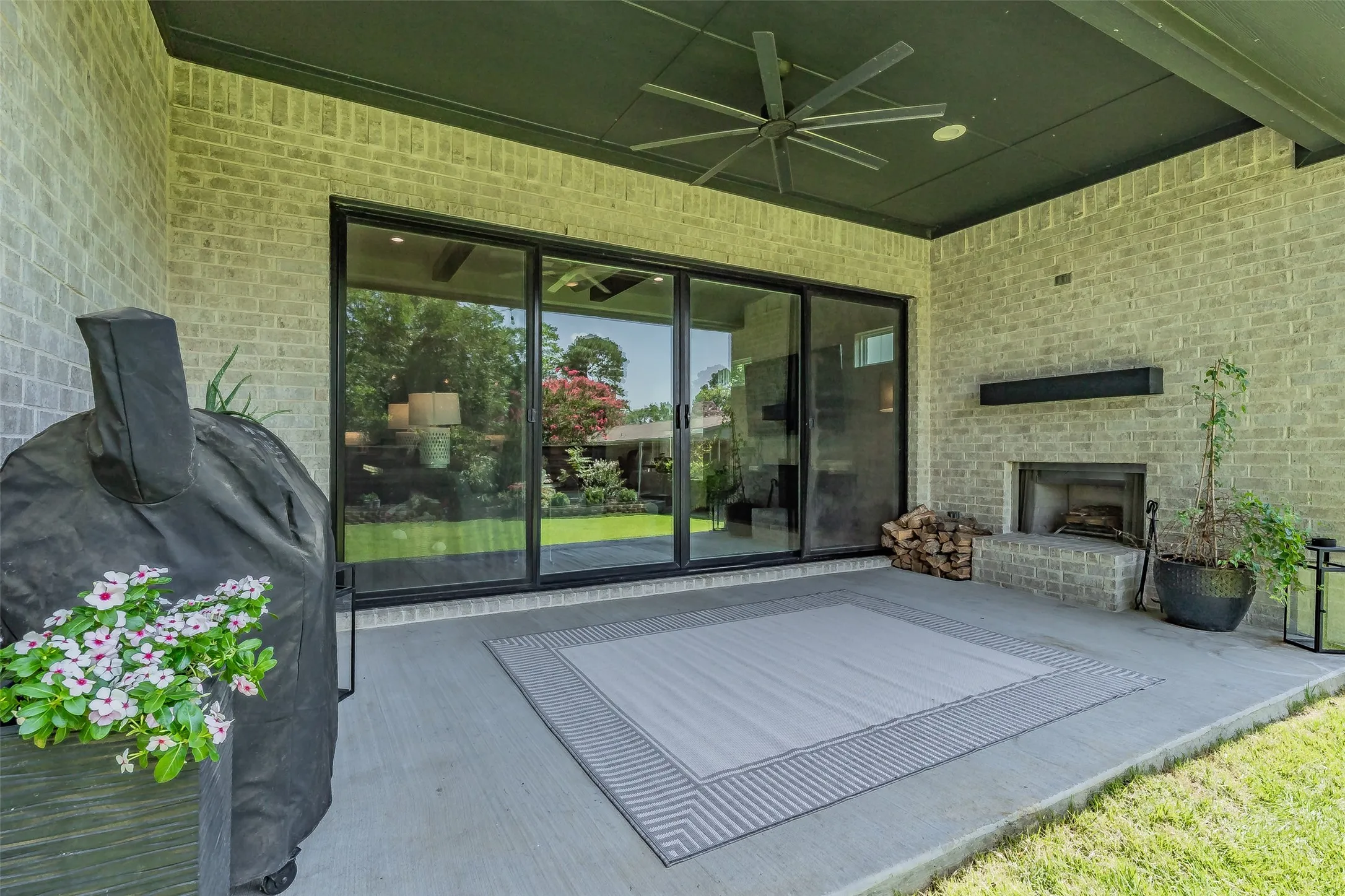 Covered outdoor patio featuring light brickwork, a built-in fireplace, and a black ceiling with a ceiling fan
