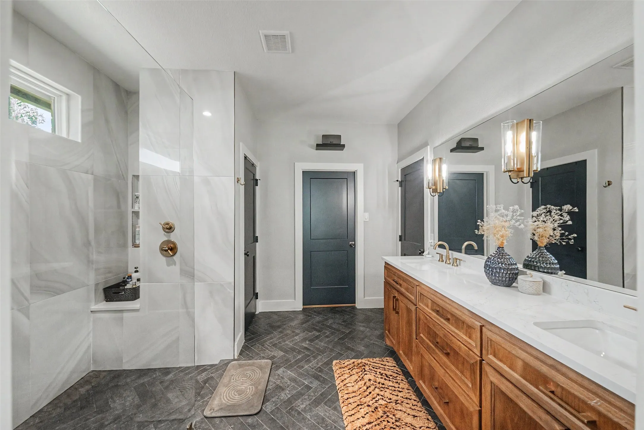 Spacious bathroom featuring a dual vanity with wood cabinetry and white countertops, a large mirror, and herringbone pattern floor tiles