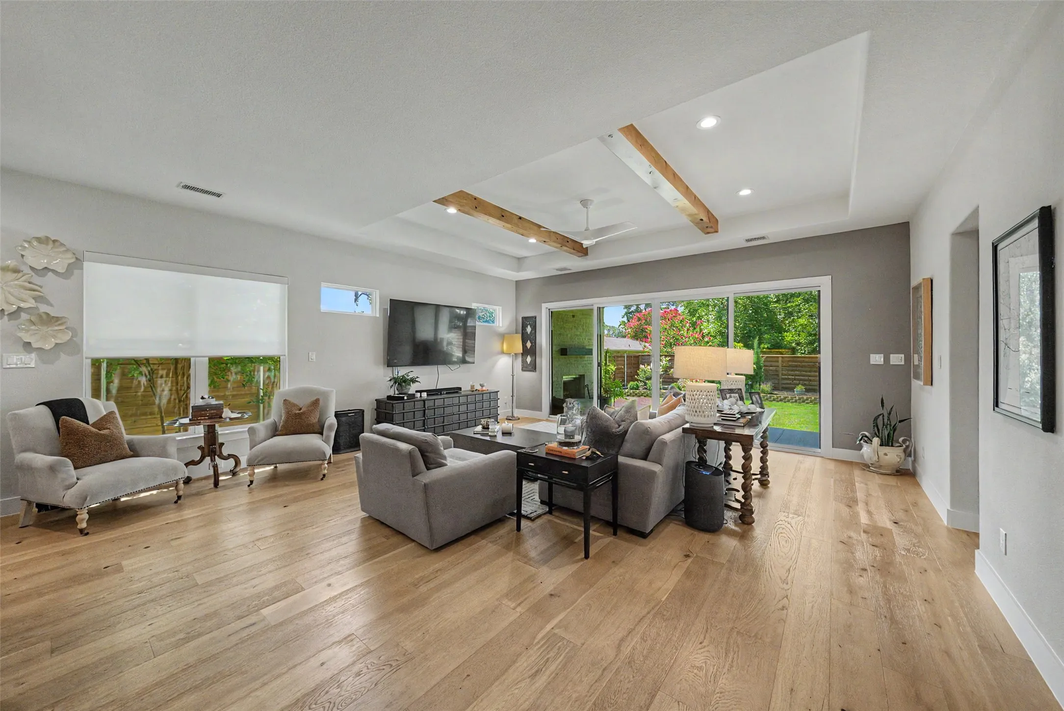 Spacious living area featuring wide-plank wood-finish flooring, a tray ceiling with wood beams, recessed lighting, and a ceiling fan