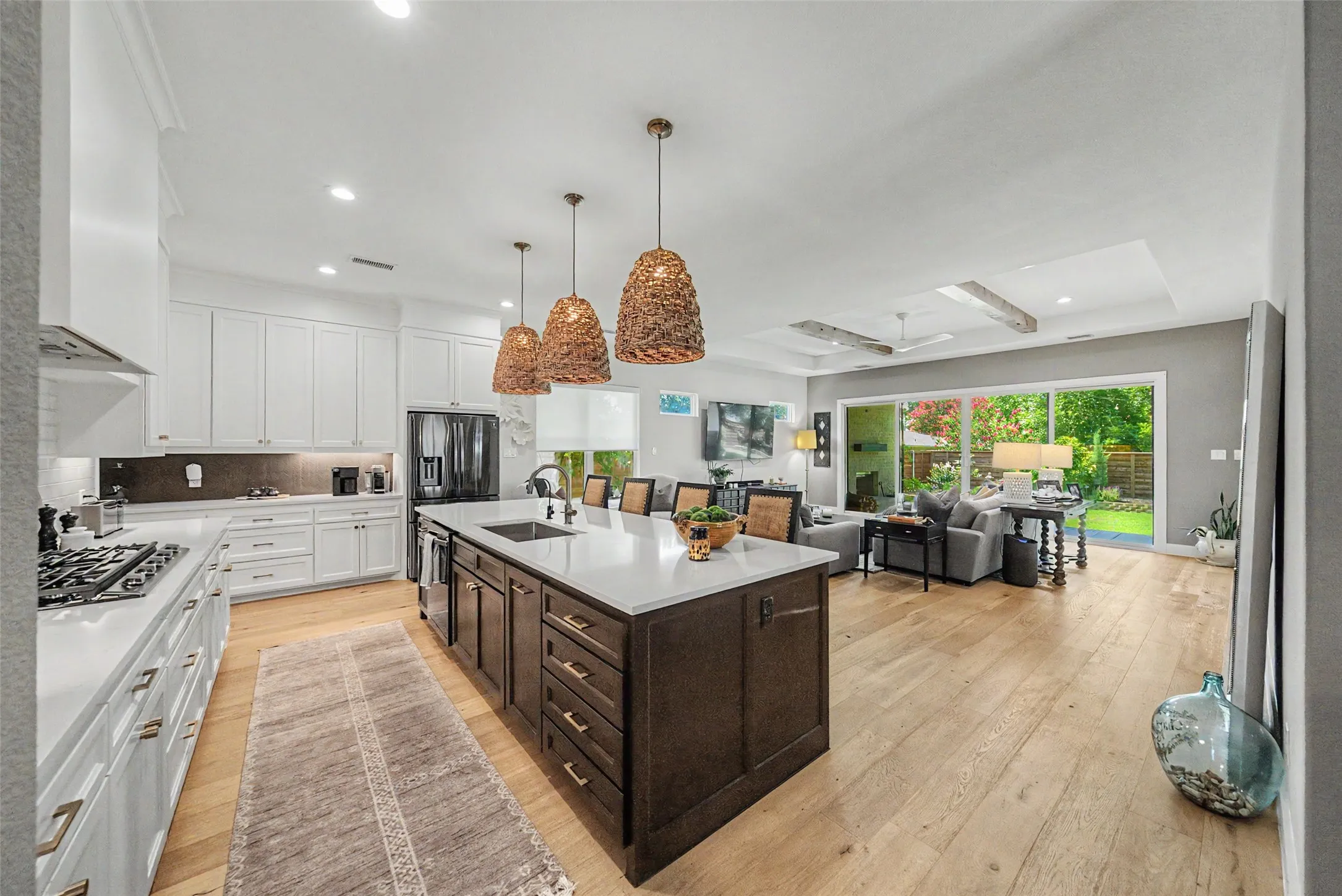 Open-concept kitchen and living area featuring a large center island, light wood-finish flooring, white cabinetry with gold-tone hardware, and a gas range