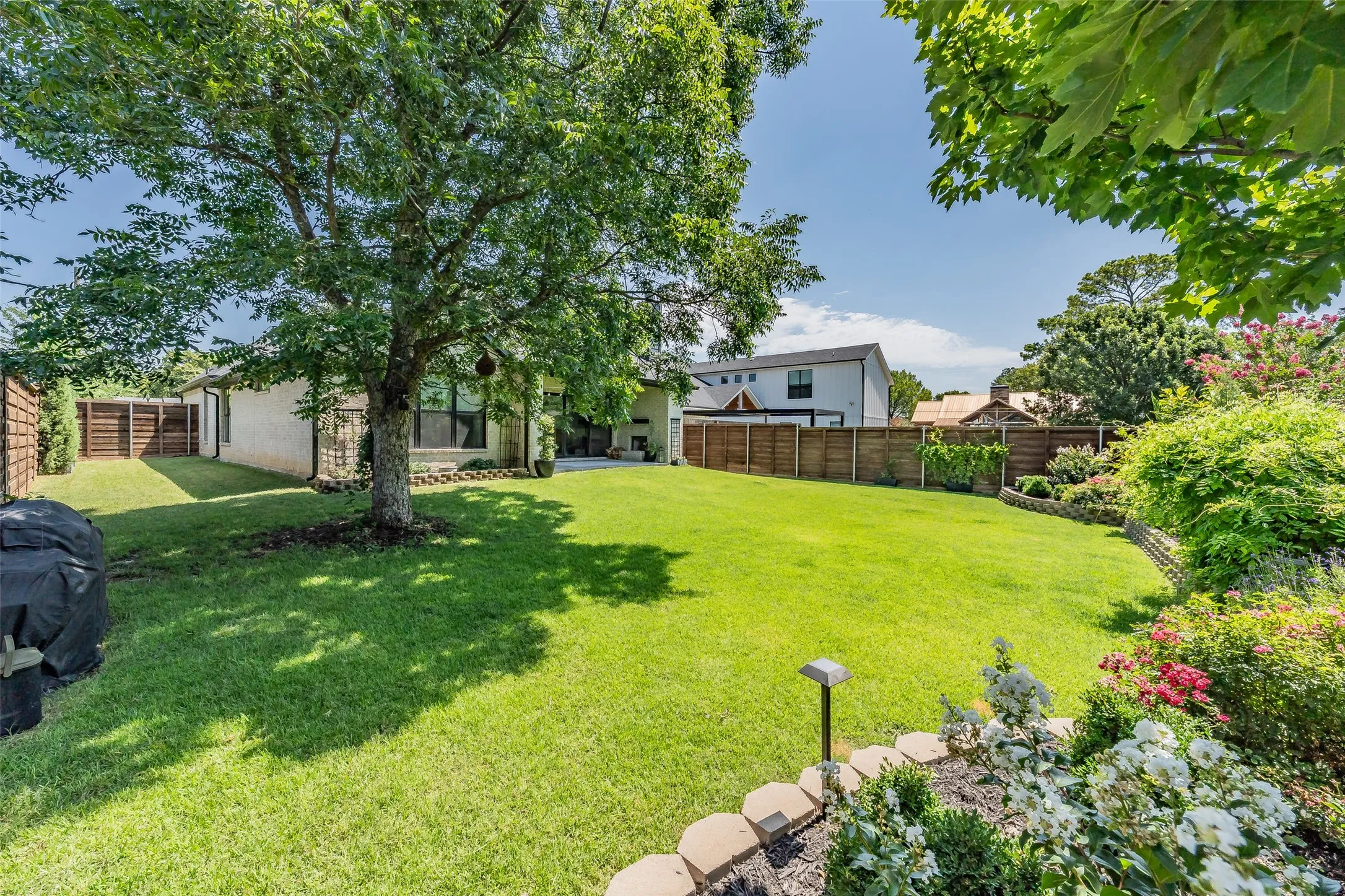 Expansive backyard featuring a manicured lawn, mature trees, and privacy fencing