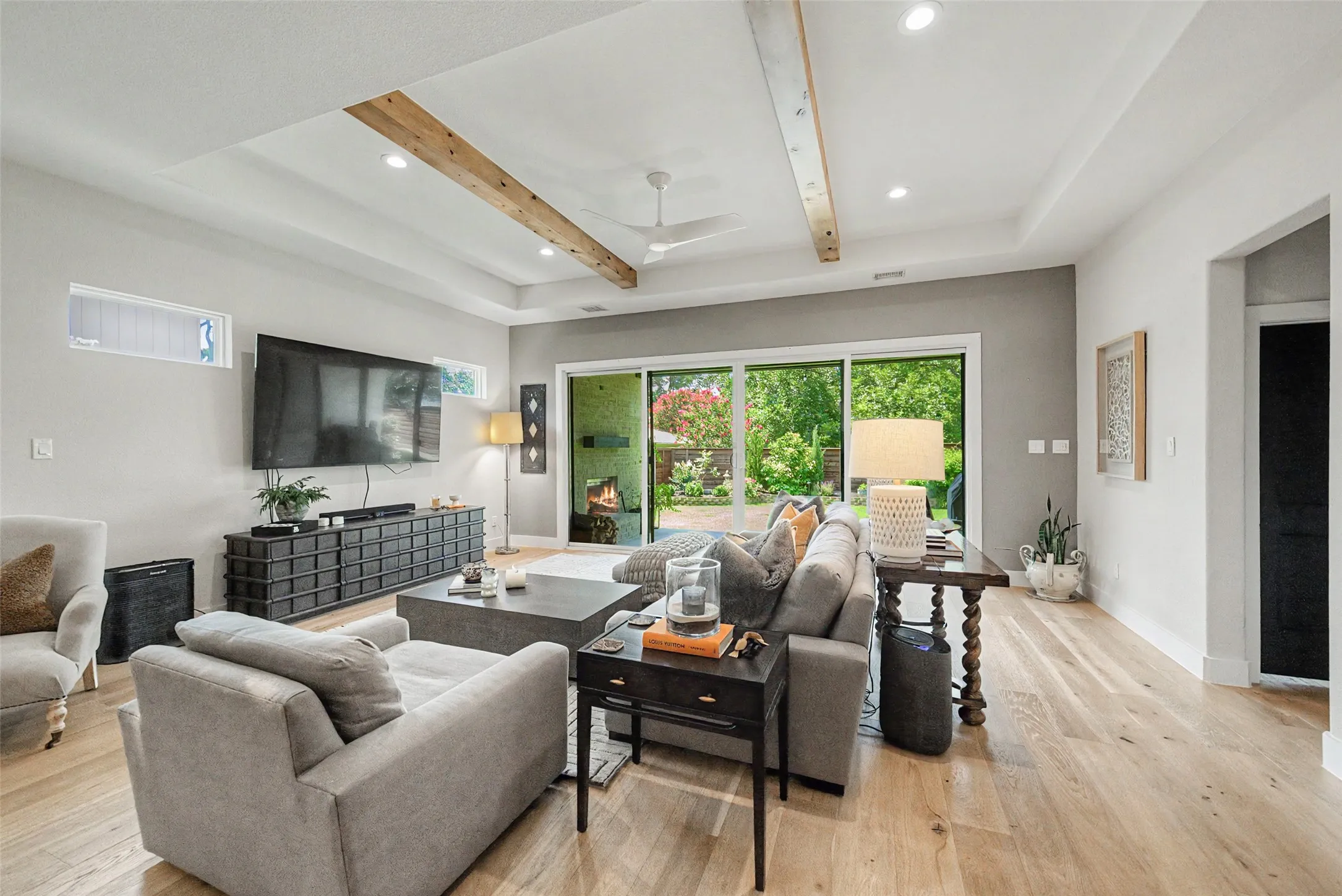 Spacious living area featuring wood-finish flooring, a tray ceiling with exposed beam accents, and recessed lighting