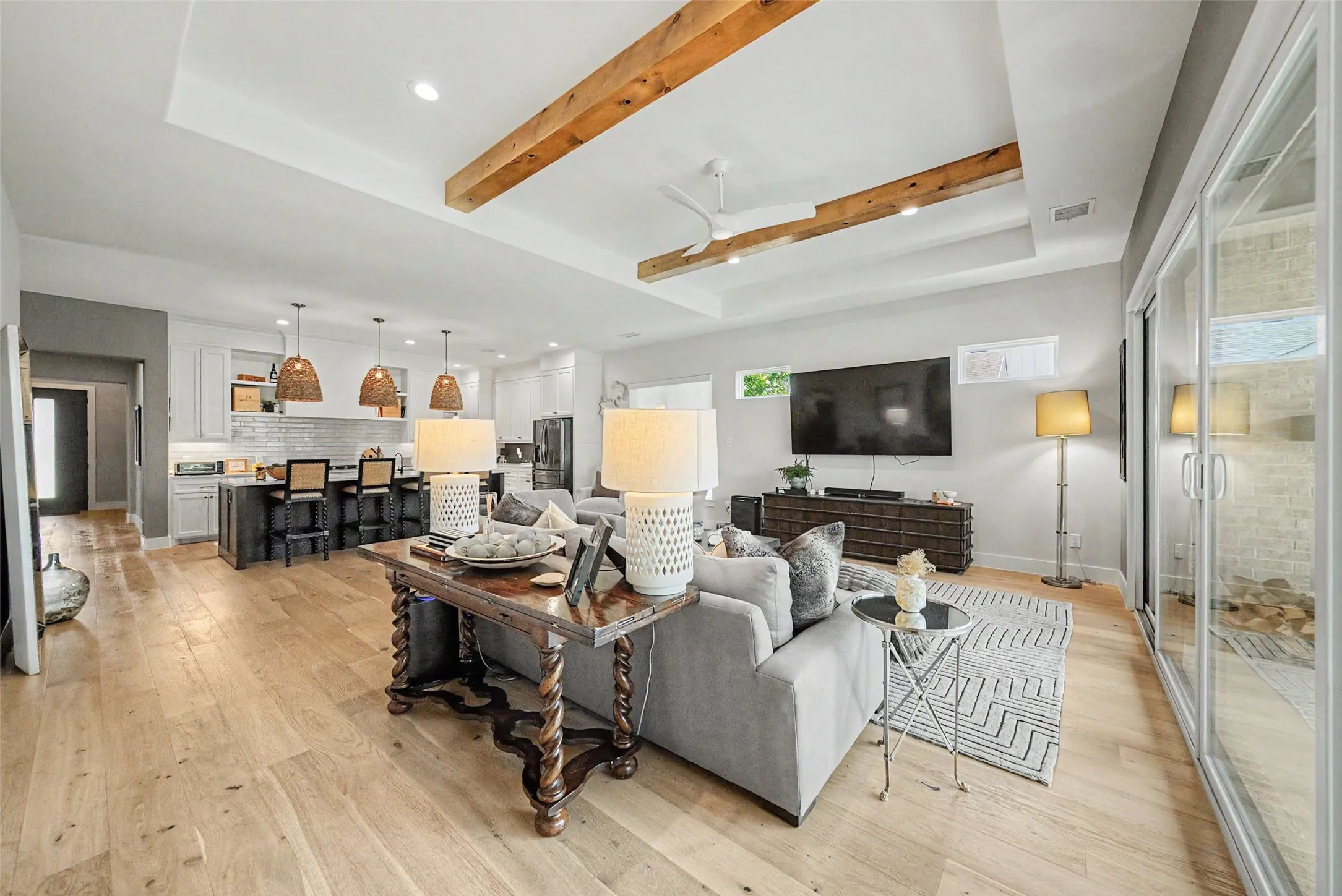 Open concept living area featuring wood-finish flooring, a tray ceiling with exposed wood beams, and a modern kitchen