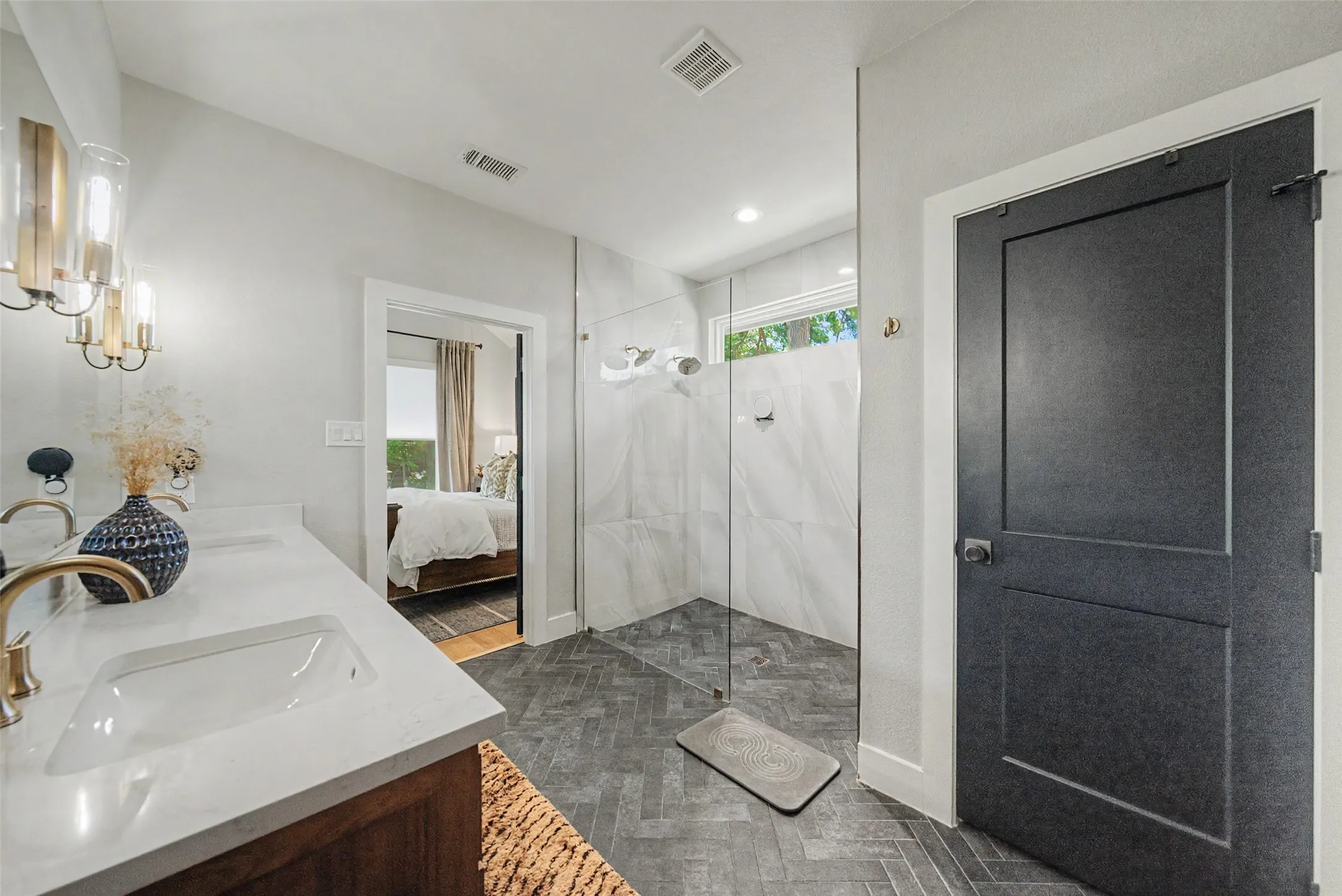 Bathroom featuring a dual vanity with undermount sinks, quartz countertops, a walk-in shower with glass enclosure, large format tile walls, and herringbone pattern floor tile