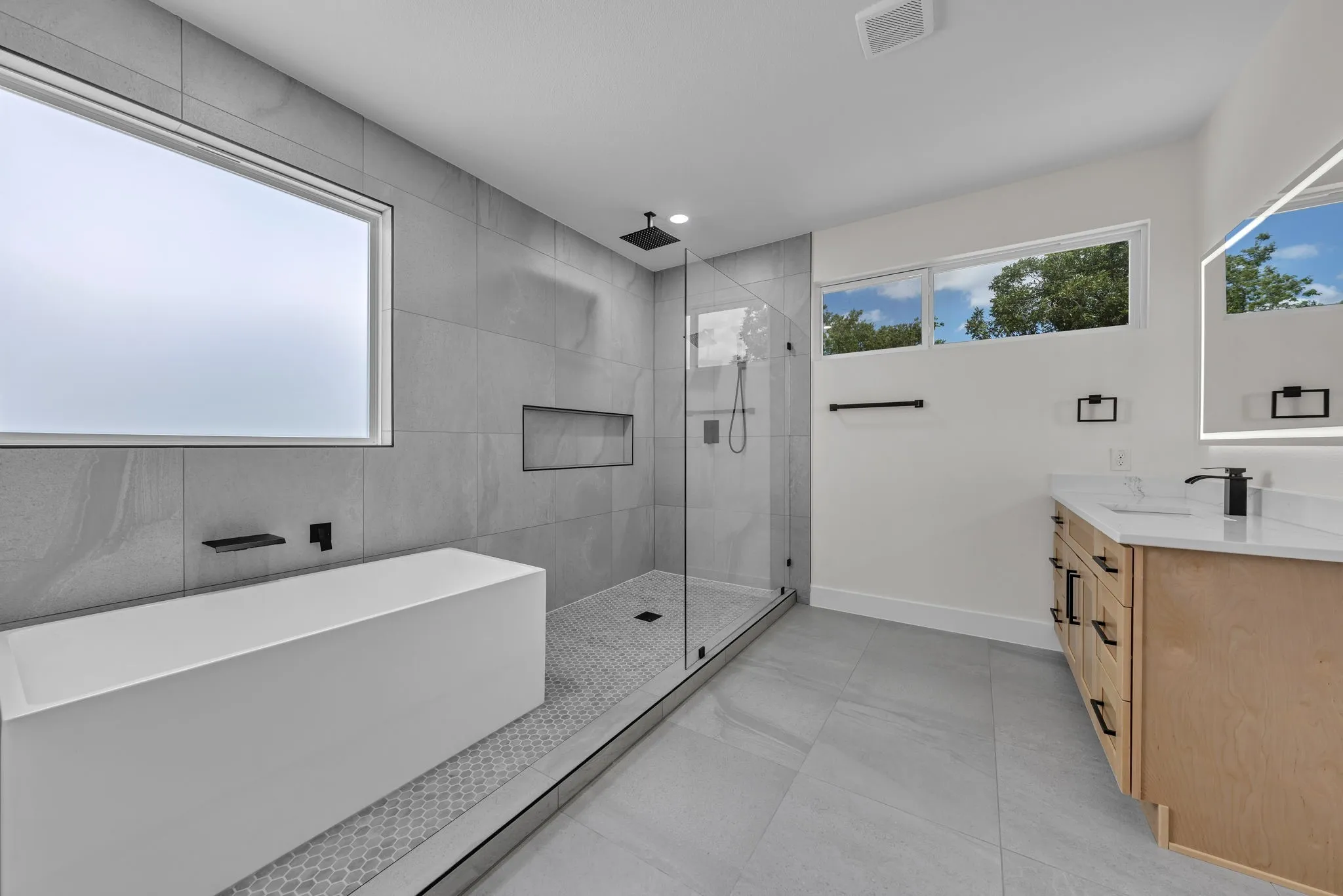 Contemporary bathroom featuring a freestanding tub, glass-enclosed shower with gray tiled walls, a wood-finish vanity with a quartz countertop, and large format gray floor tiles