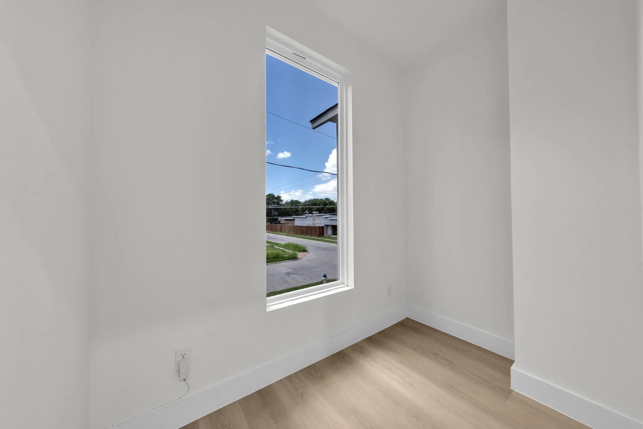 Bright interior space featuring a tall window, light wood-finish flooring, crisp white walls, and substantial baseboards