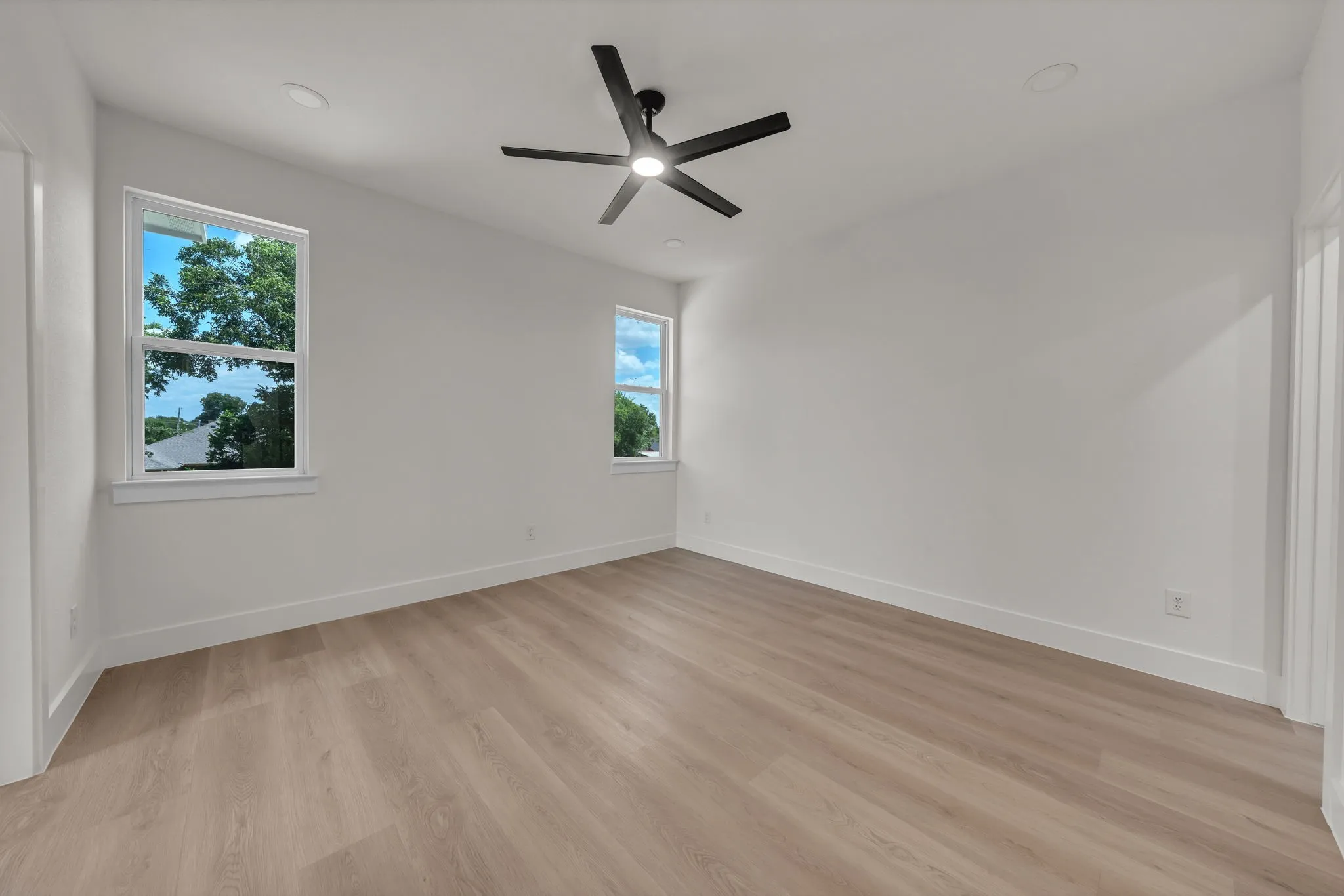 Spacious room featuring wood-finish flooring, white baseboards, and two double-hung windows