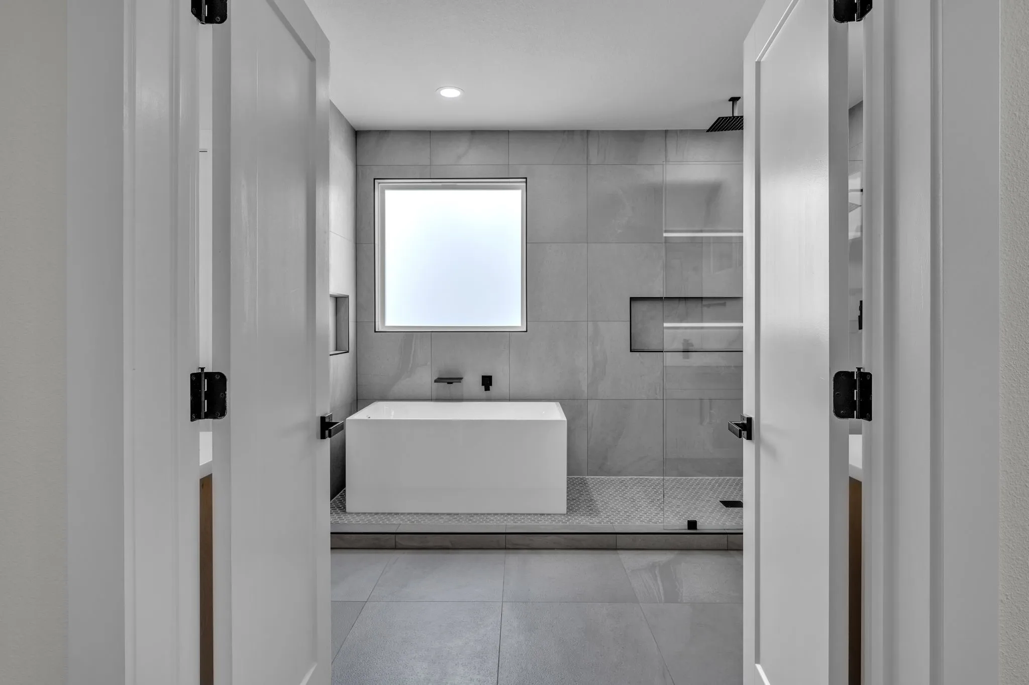 Contemporary bathroom featuring a freestanding soaking tub, large format tile flooring, and a glass-enclosed shower with a rainfall showerhead