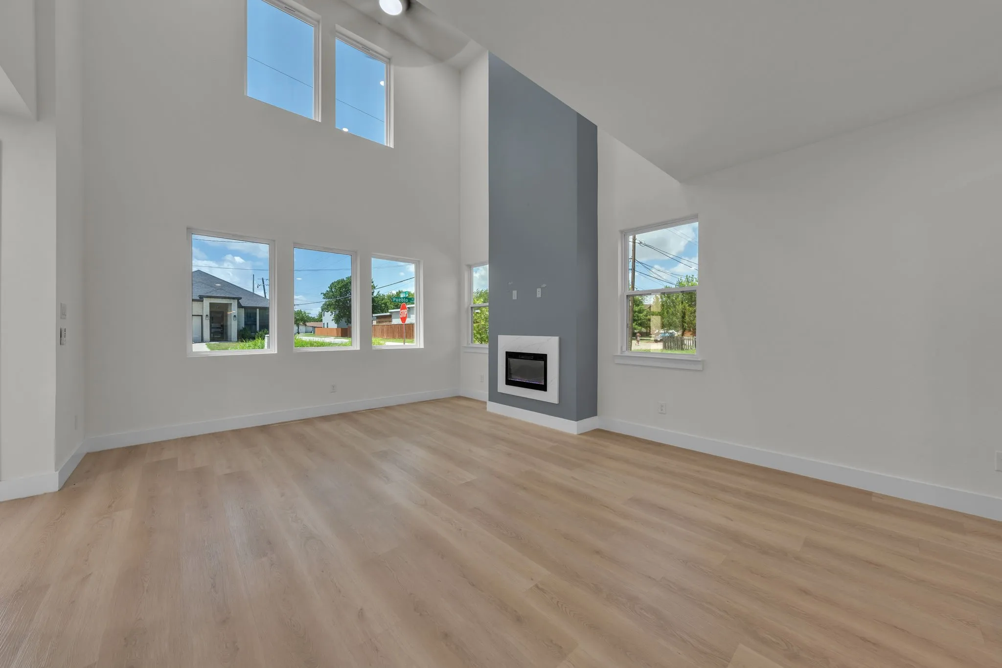 Spacious living area featuring high ceilings, light wood-finish flooring, and multiple windows providing ambient light