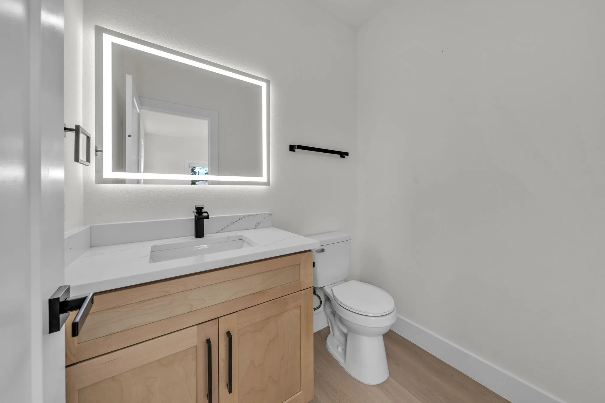 Bathroom vanity featuring a lighted mirror, a rectangular undermount sink, a stone-finish countertop, and a wood-finish cabinet with black hardware