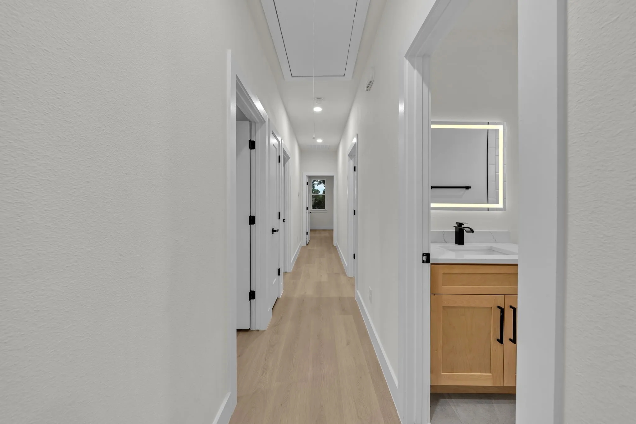 Hallway featuring light wood-finish flooring, recessed lighting, and crisp white walls
