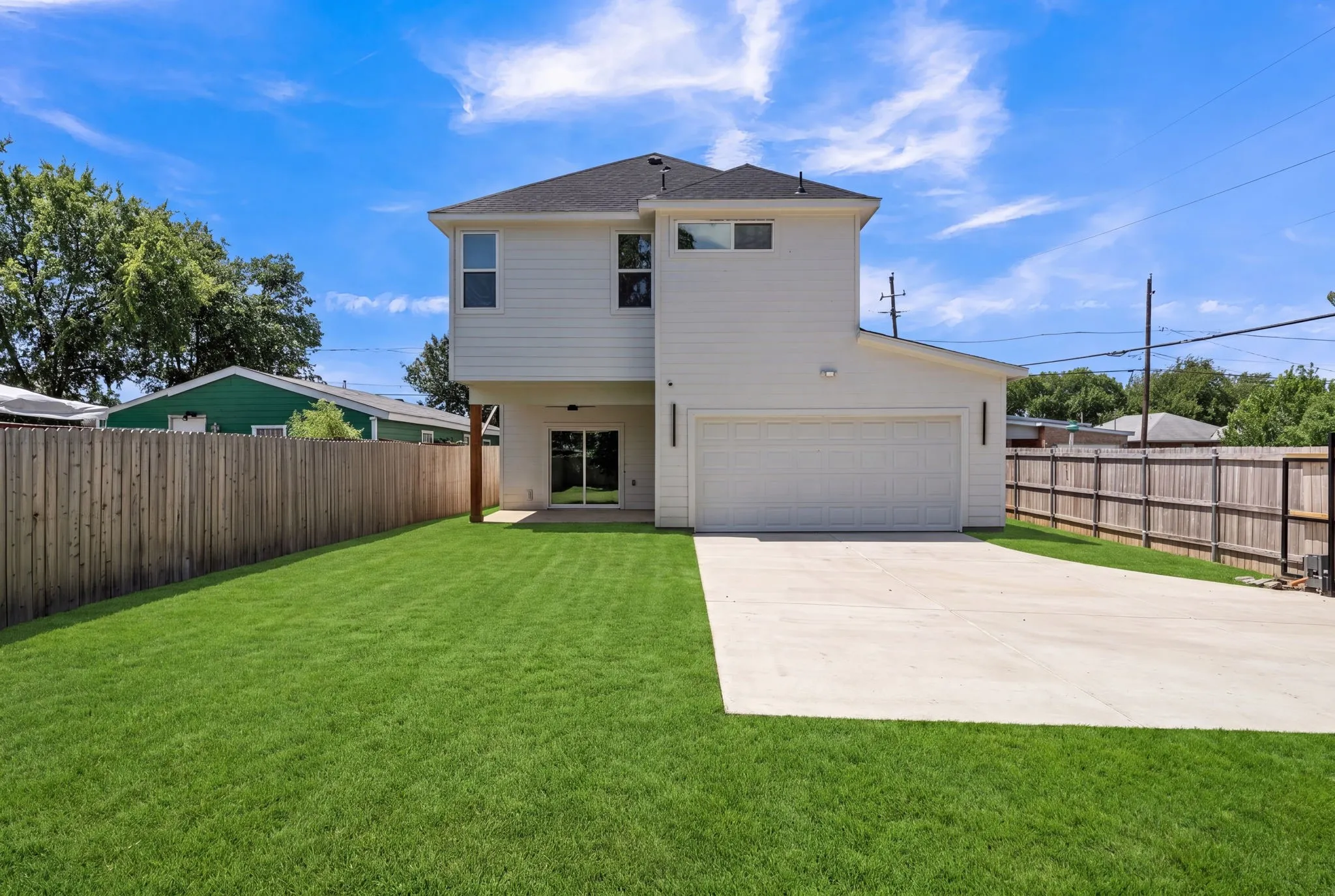Rear exterior featuring a two-story white facade, dark shingle roof, and an attached two-car garage