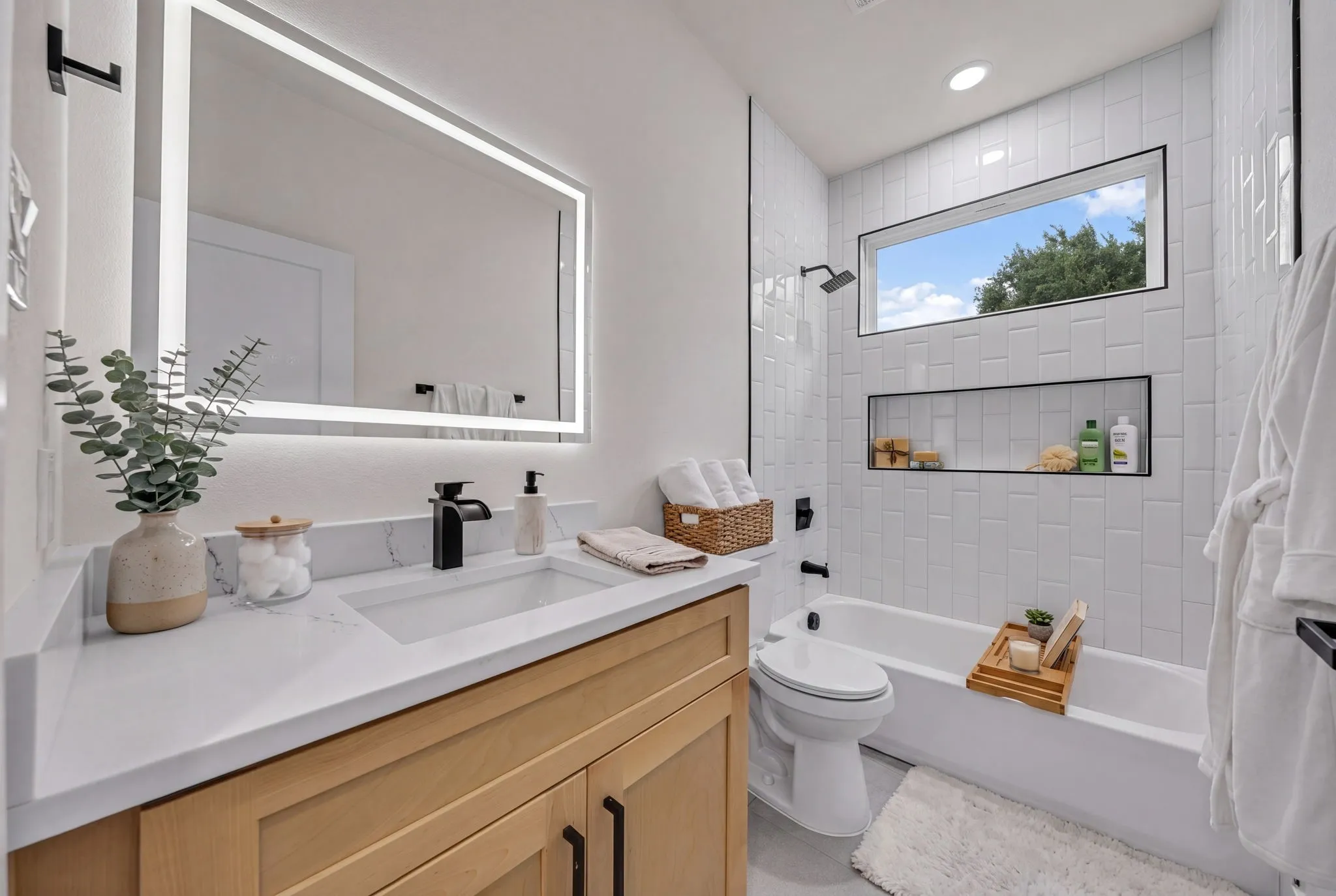 Bathroom featuring a light wood-finish vanity with a white countertop and rectangular undermount sink, complemented by a lighted mirror and matte black fixtures