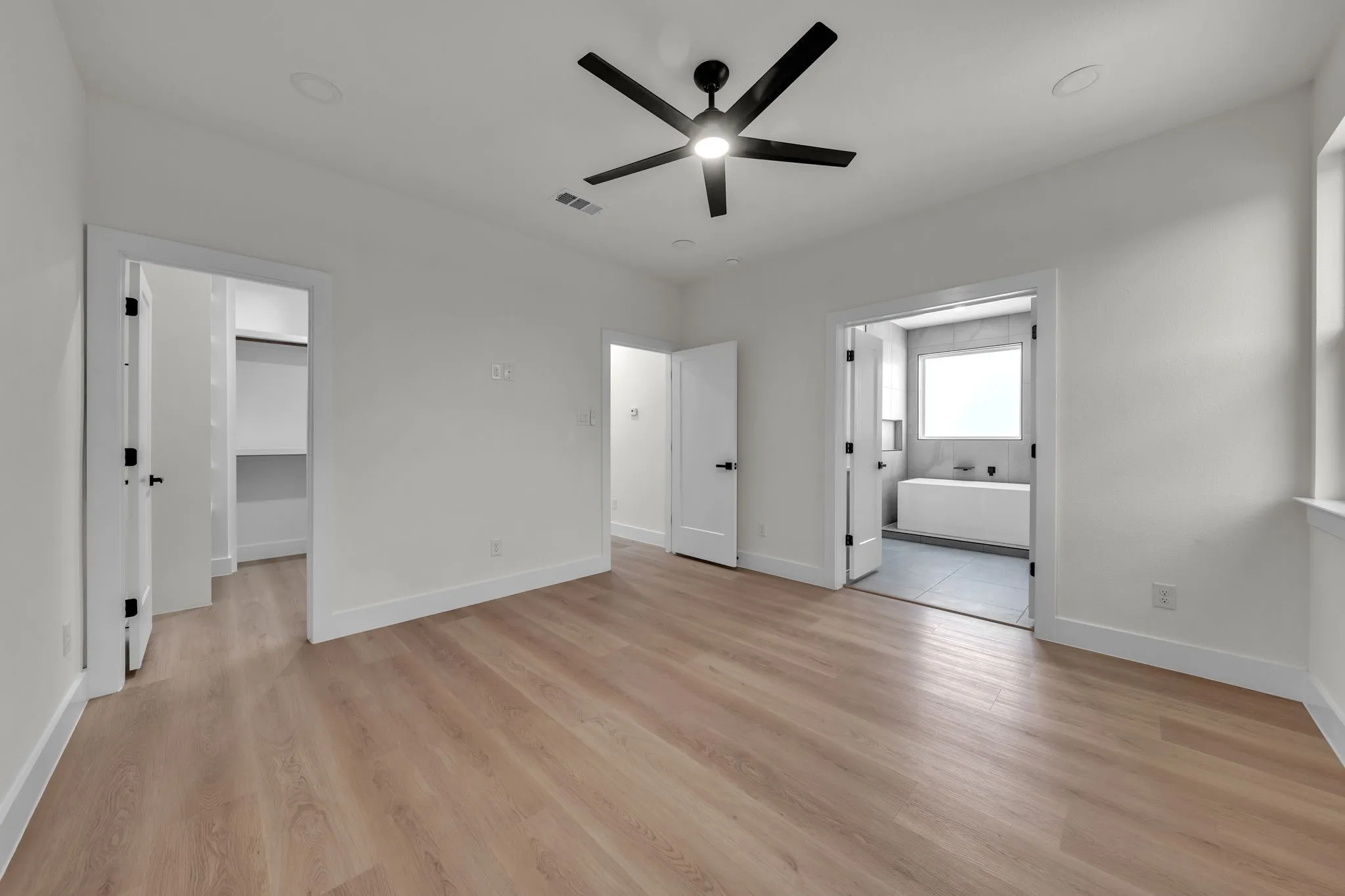 Spacious room featuring wood-finish flooring, white walls, and a contemporary ceiling fan