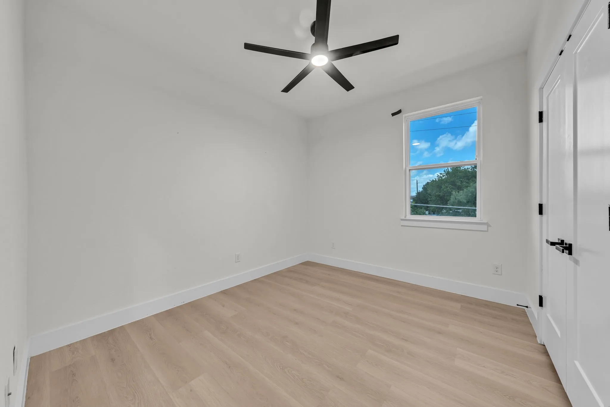 Bright interior space featuring wood-finish flooring, white baseboards, and a modern ceiling fan