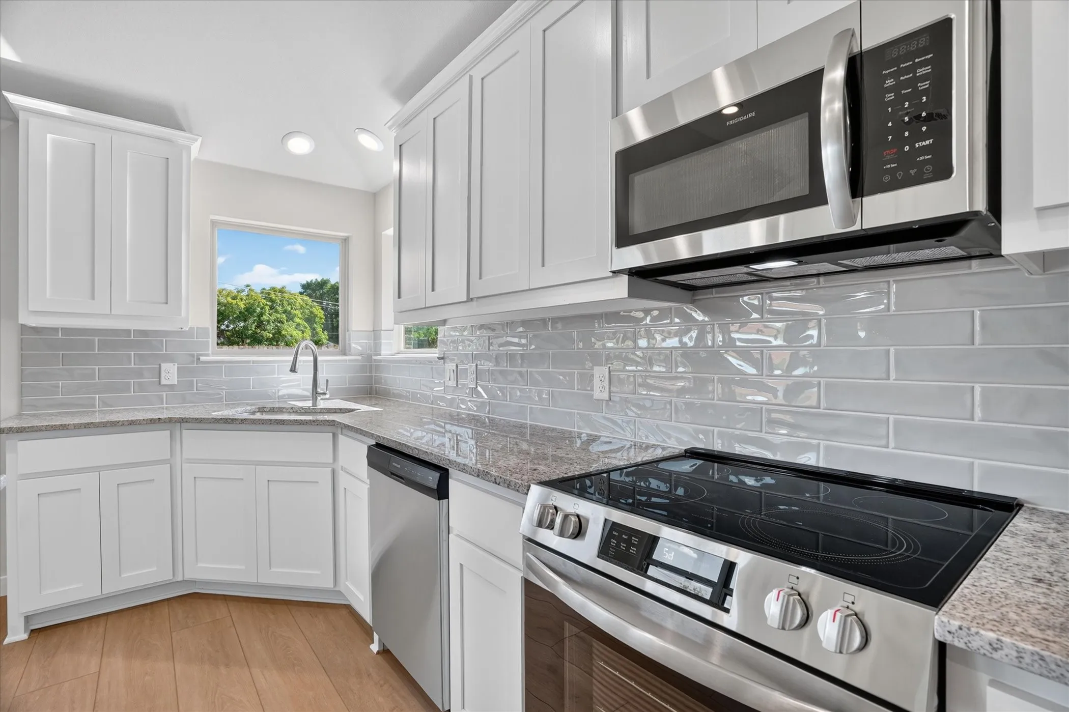 White shaker cabinetry, quartz countertops, subway tile backsplash, stainless steel appliances, and wood-finish flooring