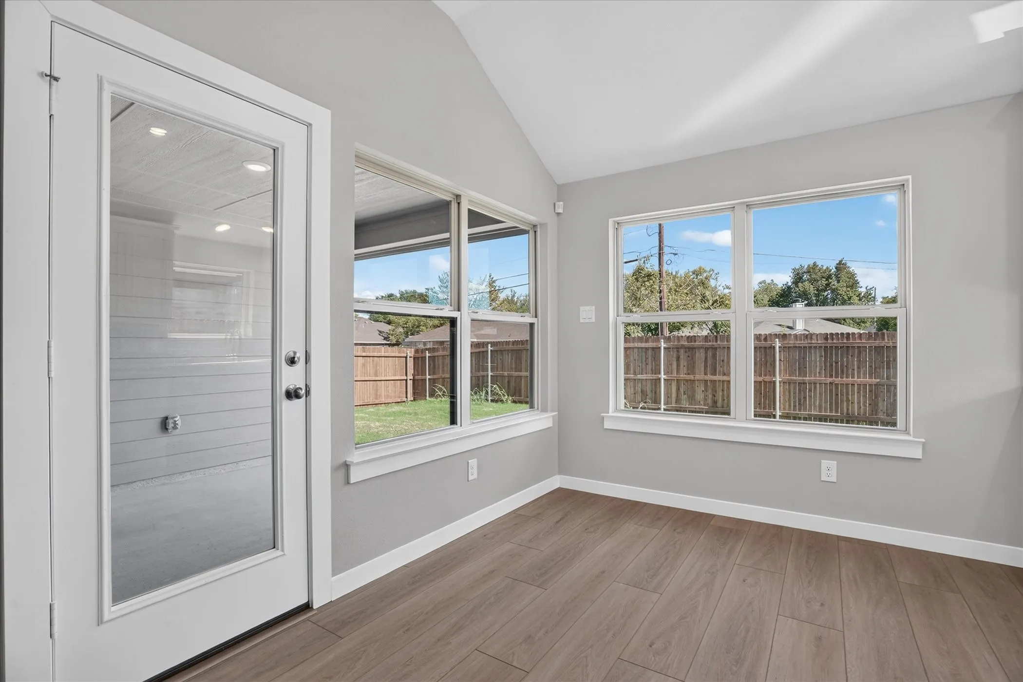 Vaulted ceiling with recessed lighting, wood-finish flooring, multiple windows, and a glass-paneled door
